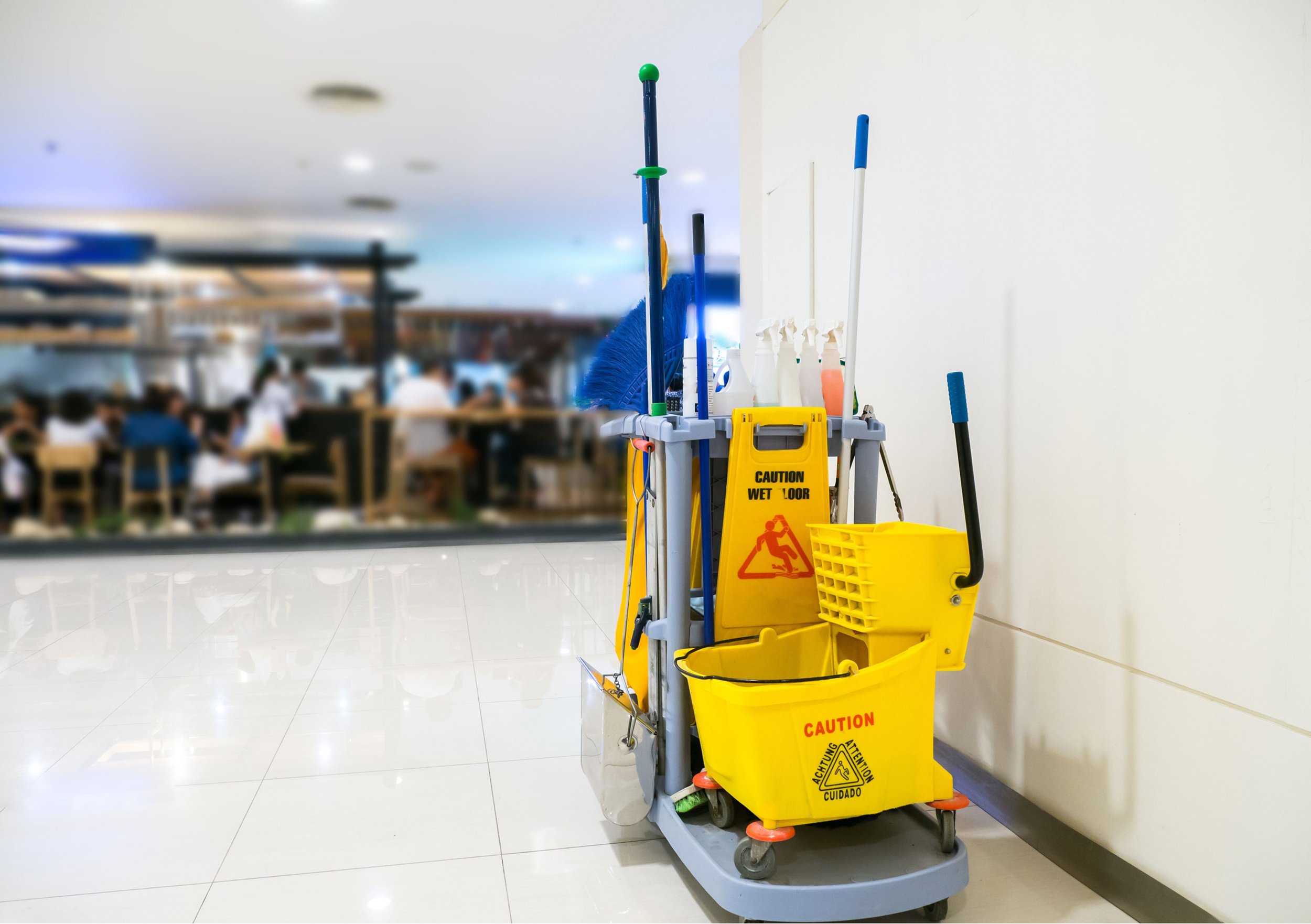 Cleaning cart with mop, broom, and cleaning supplies in a shopping mall or food court.