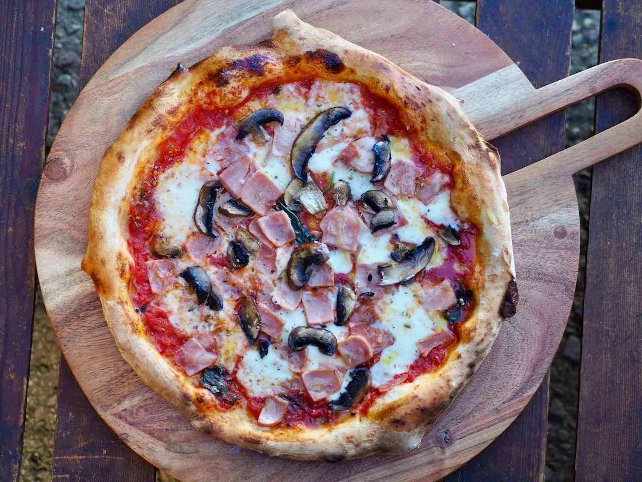 A pizza with mushrooms, ham, and cheese on a wooden serving board.