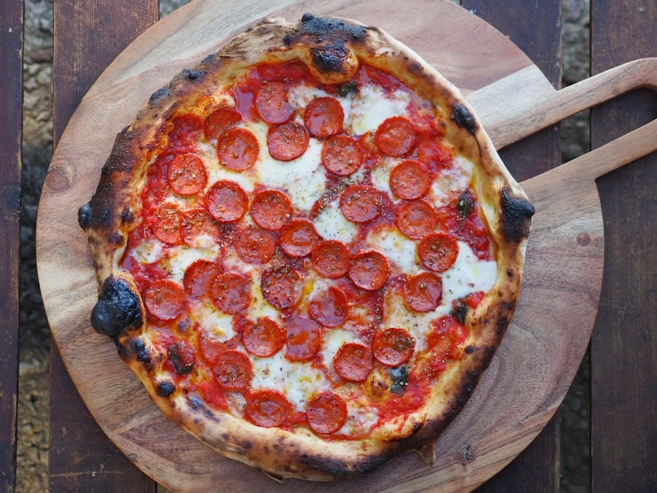 Pizza with pepperoni slices on a wooden serving board.