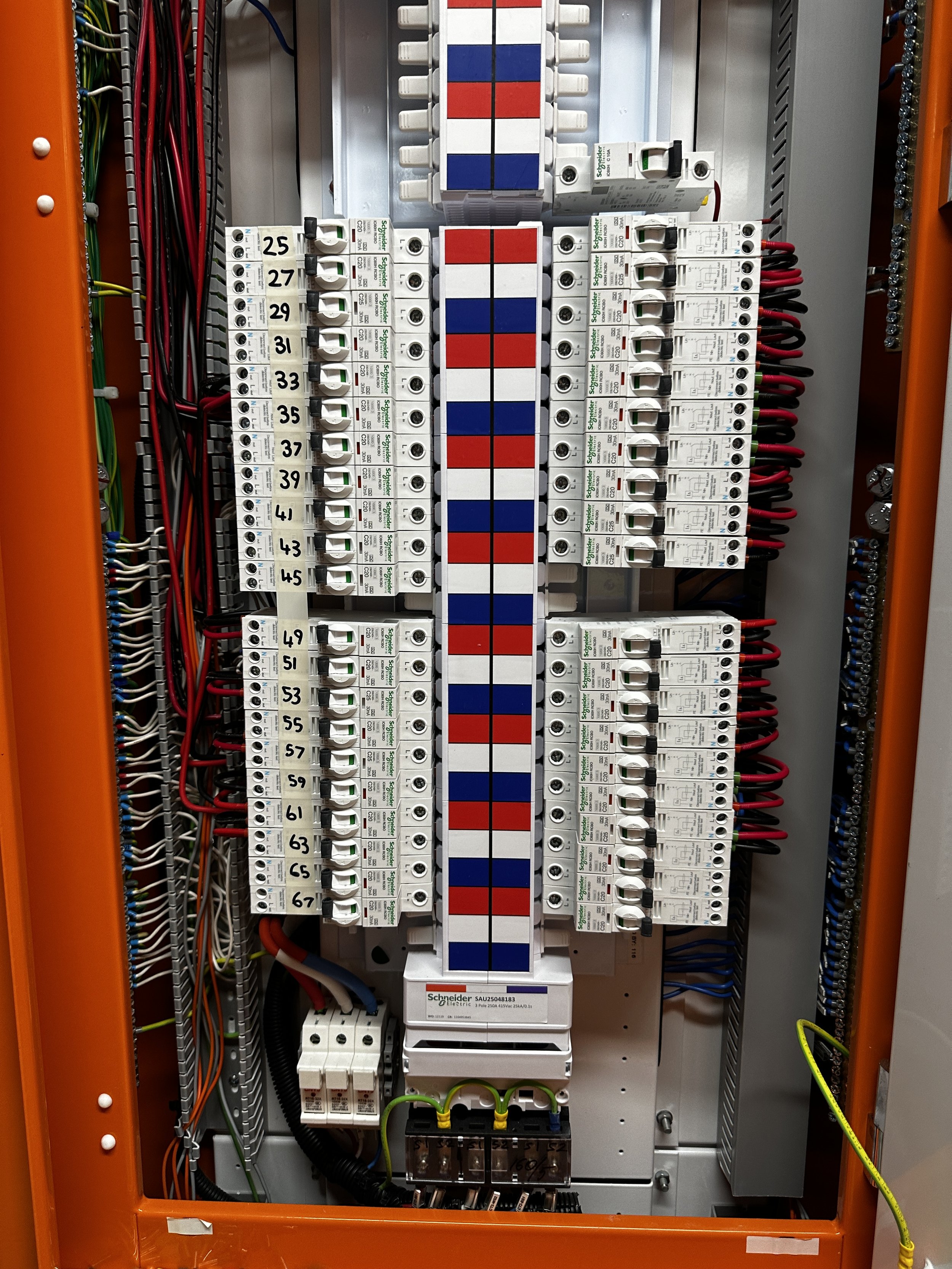 Electrical control panel with white, red, and blue wiring and components, including circuit breakers and switches, inside an orange metal enclosure.