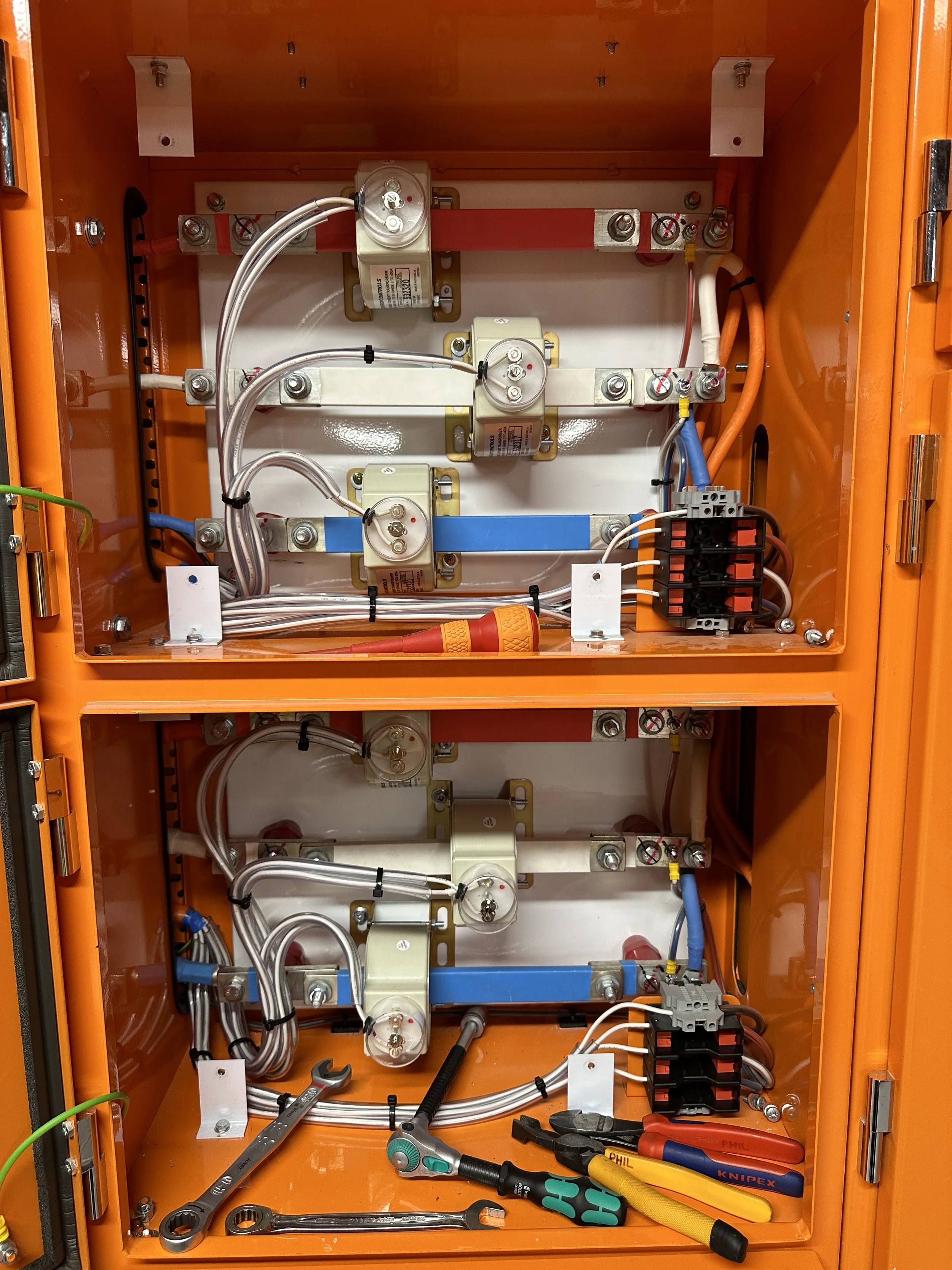 Inside an orange electrical cabinet with various wires, circuit breakers, and electrical components, along with tools like screwdrivers, pliers, and wrenches placed inside.