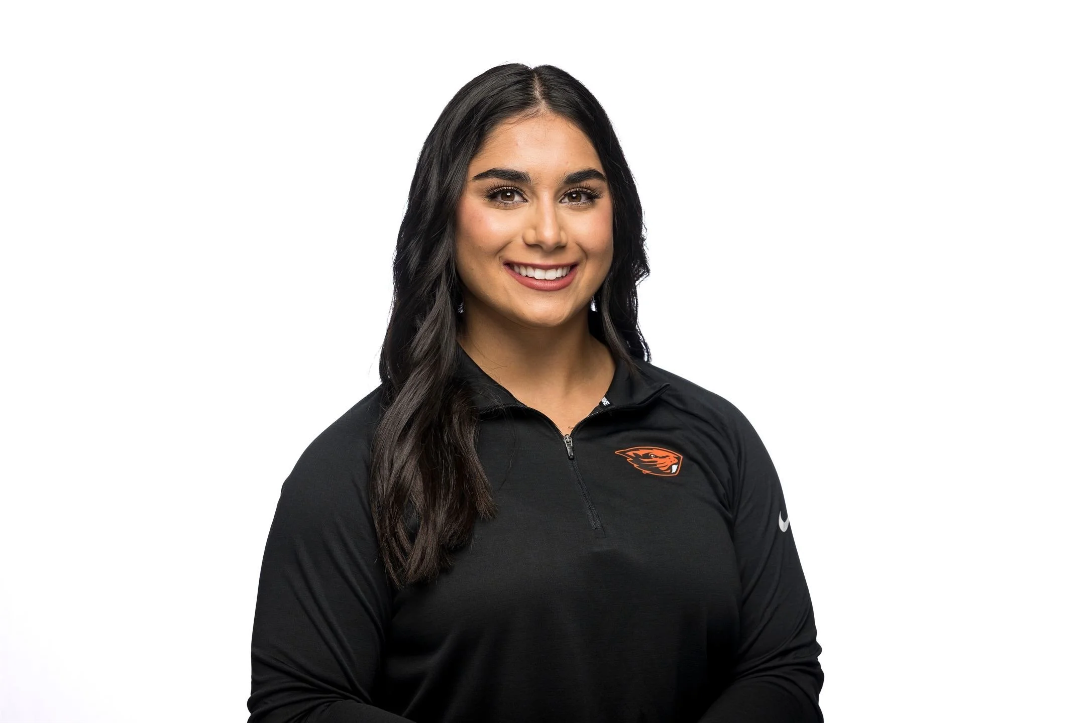 Portrait of a young woman with long dark hair, wearing a black zip-up athletic shirt with a sports team logo, smiling against a white background.