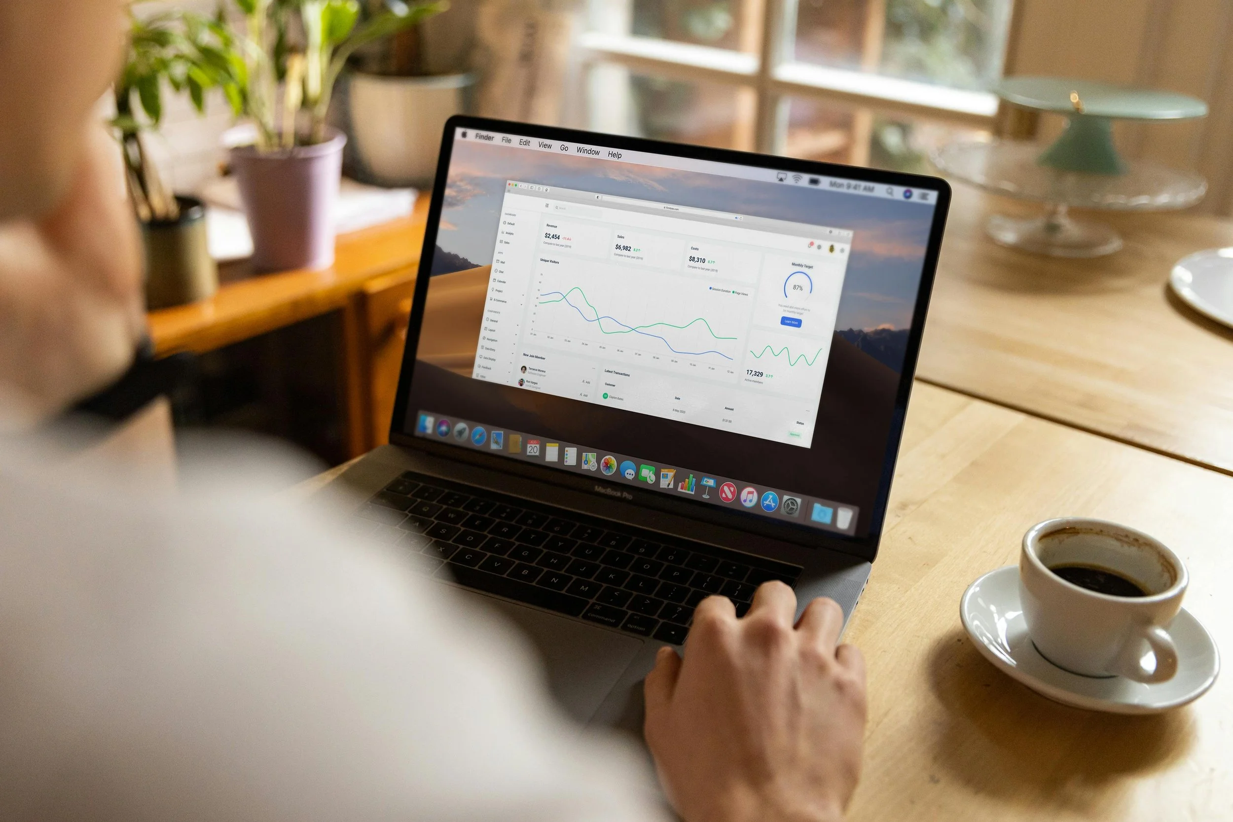 Person working on a laptop displaying financial or analytics data, with a cup of coffee on a wooden table.