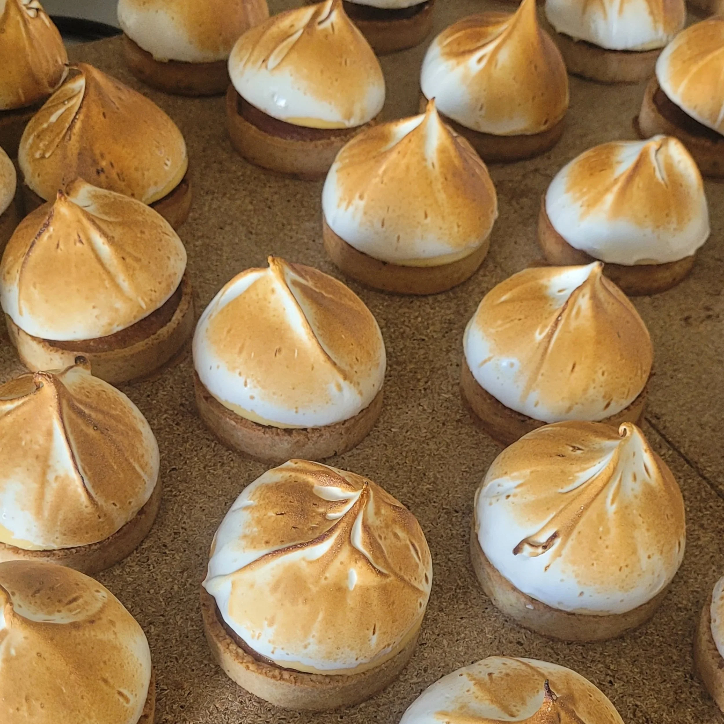 Tartelettes au citron avec un dessus grillé et doré, disposées sur une plaque de cuisson.
