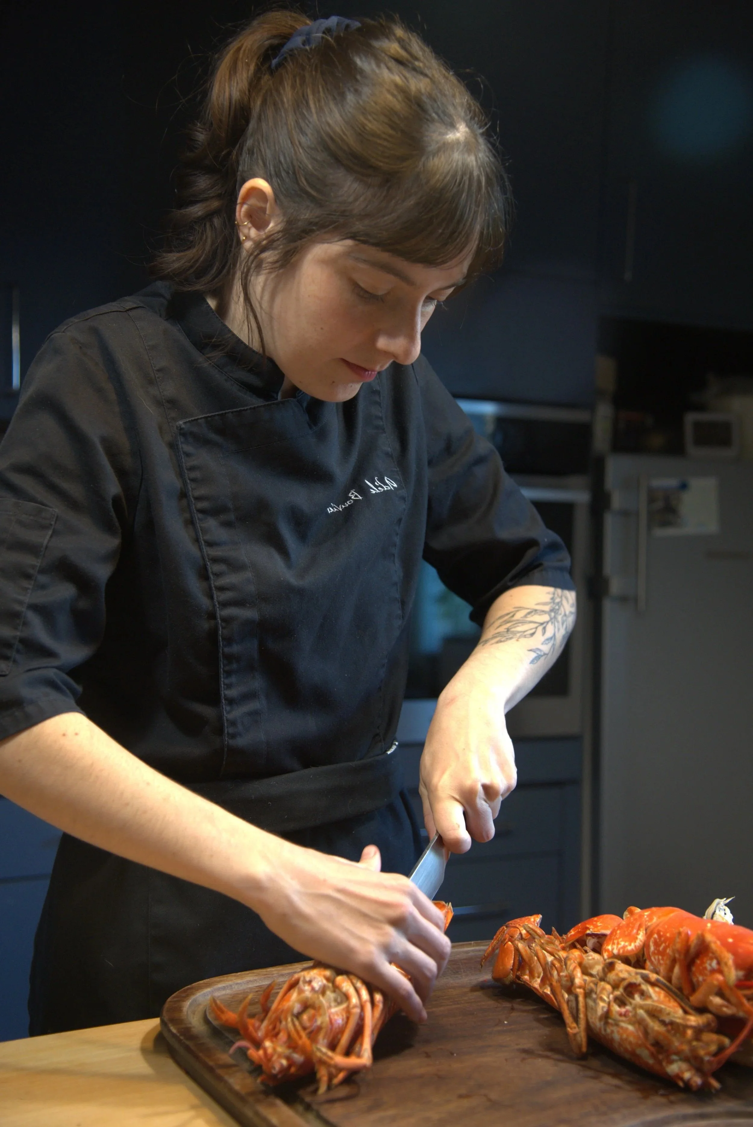 Une femme en uniforme de cuisine découpe un homard sur une planche en bois dans une cuisine.