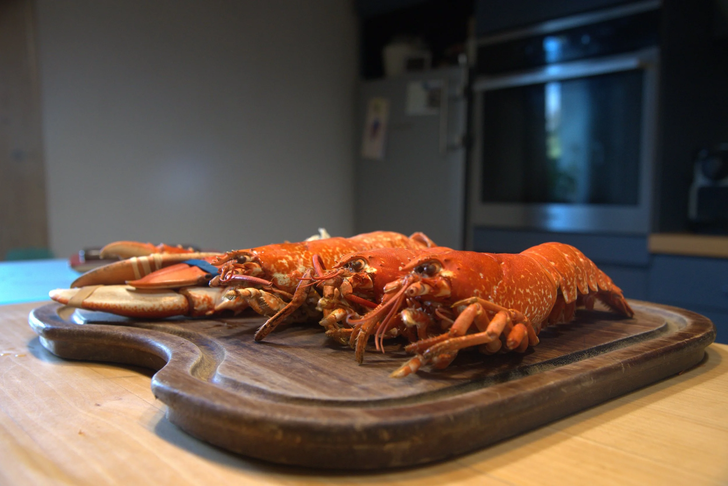 Deux homards rouges sur une planche en bois dans une cuisine.