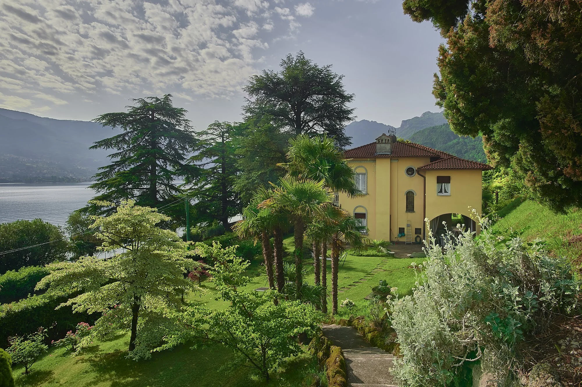 Villa Ucci sul lago di Como circondata da alberi verdi con vista su lago e montagne sullo sfondo