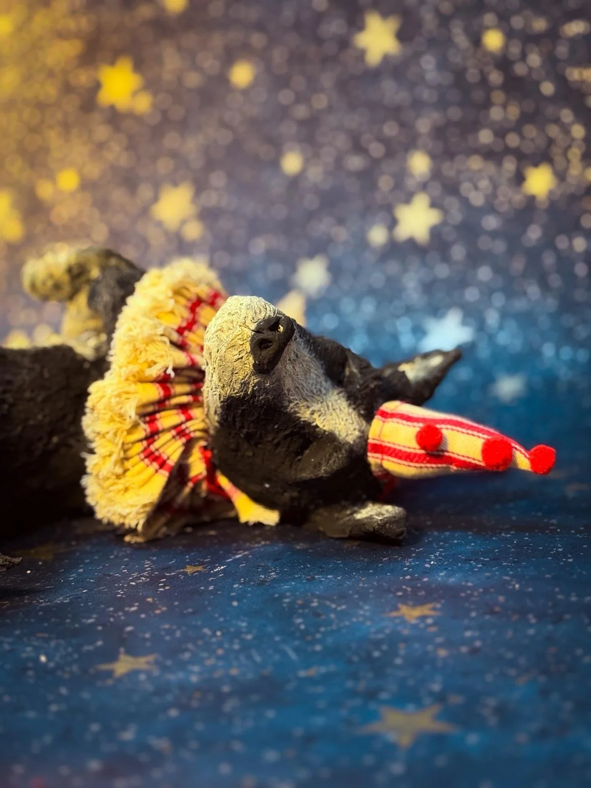 Close-up of a small dogsculpture with a fuzzy yellow and red fabric decoration, set against a dark blue background decorated with stars.