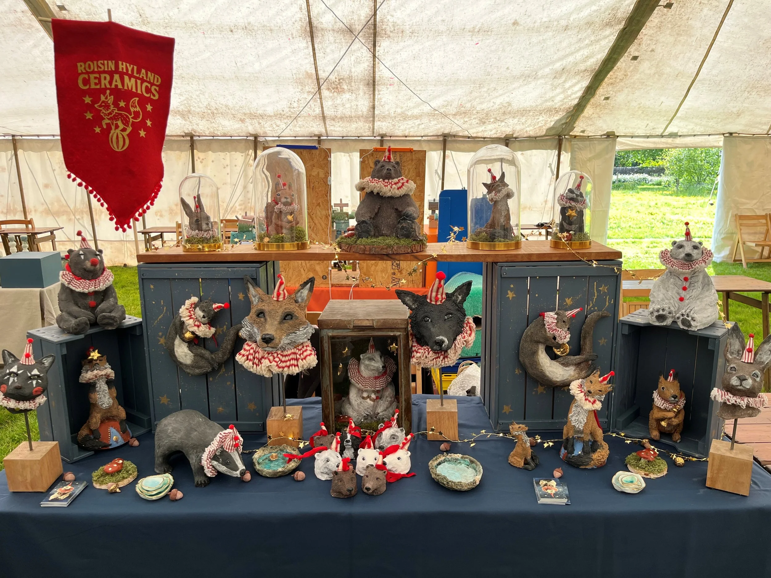 Display table with various animal sculptures wearing red and white Christmas-themed accessories inside a tent with grass outside.