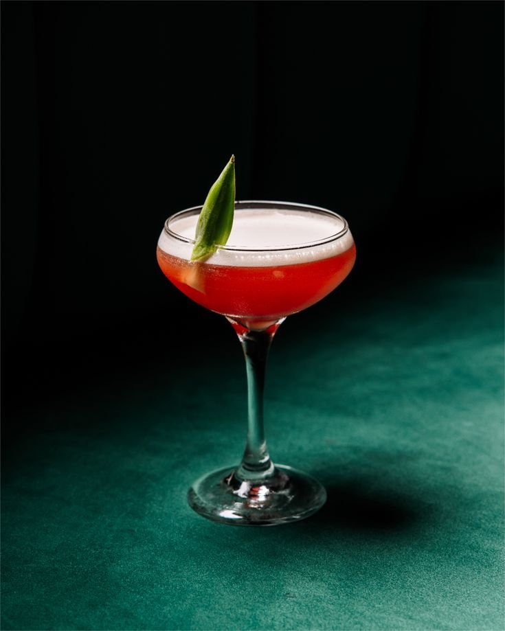 Cóctel rosa en copa de cóctel con adorno de hoja verde en el borde