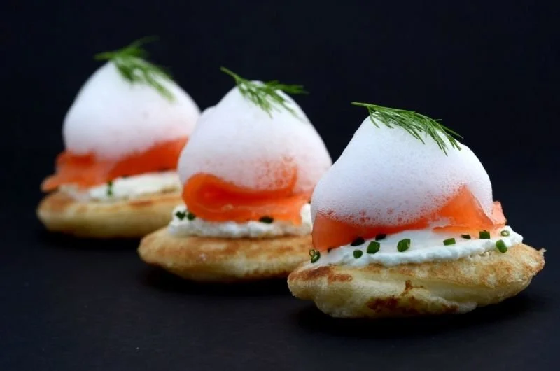 Tres aperitivos con base de pan, crema, salmón y una rama de eneldo en la parte superior.