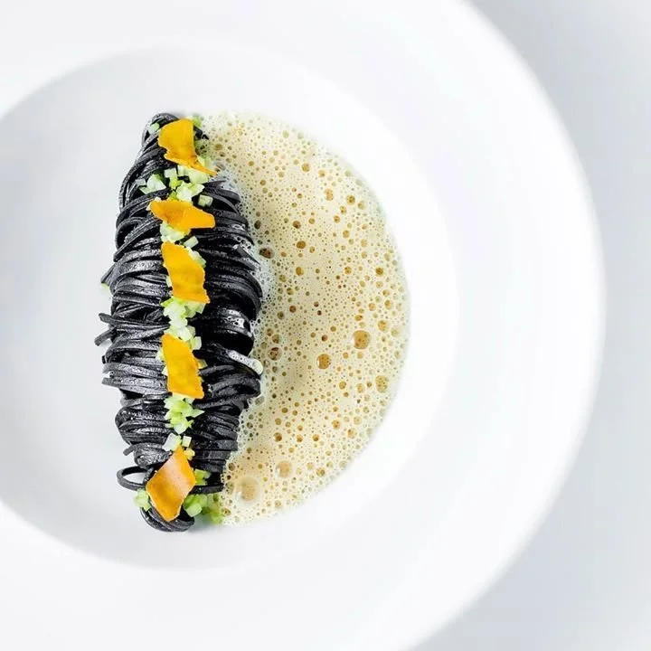 Espaguetis negros con verduras, cubiertos con espuma de sopa o caldo en un plato blanco