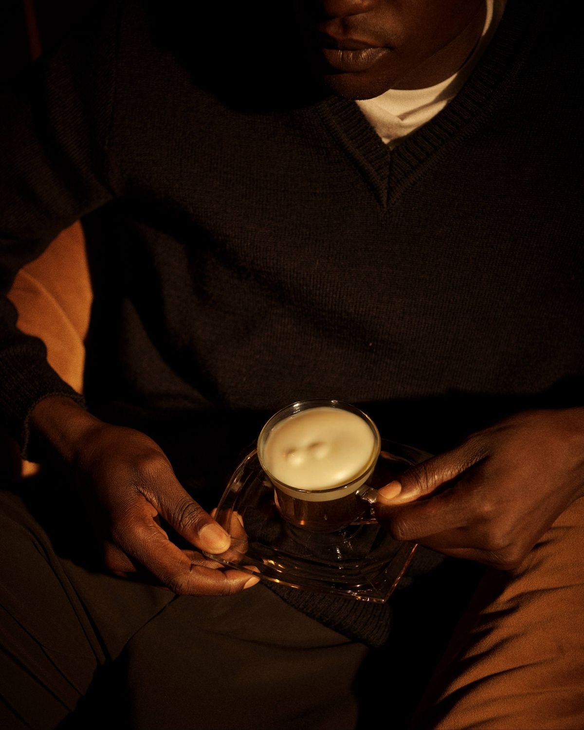 Persona sosteniendo una taza con una bebida cremosa, en un ambiente con iluminación cálida.