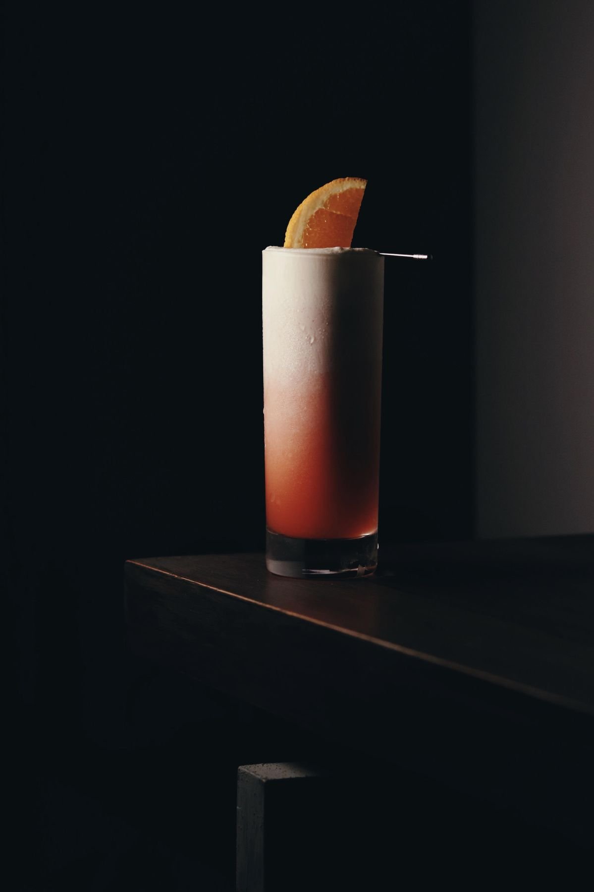 Cóctel rosado en un vaso alto con adornado de una rodaja de naranja.