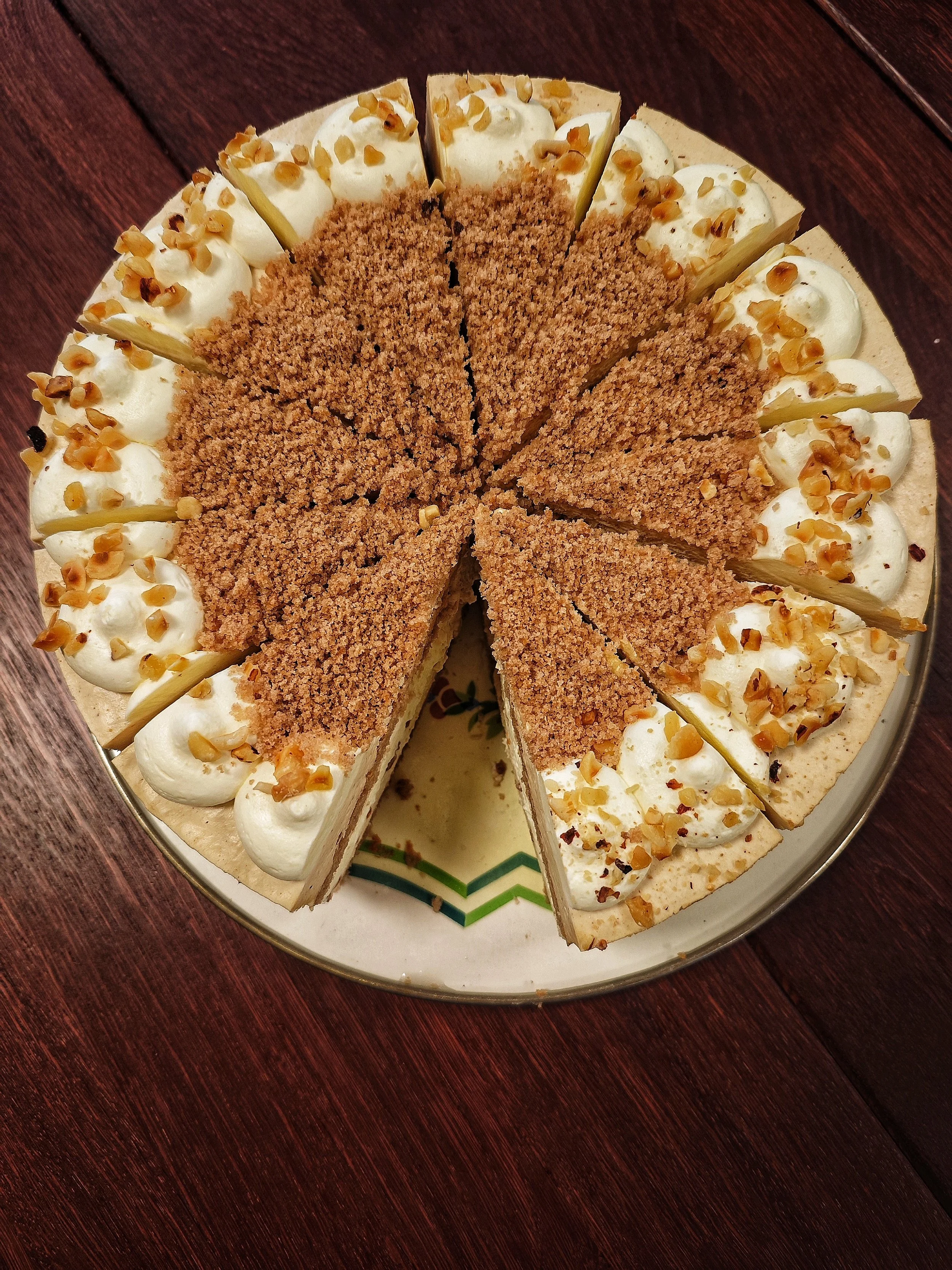 Kuchen mit einer Krümelschicht, weißen Sahnehauben mit Mandeln oben, einige Stücke sind geschnitten.