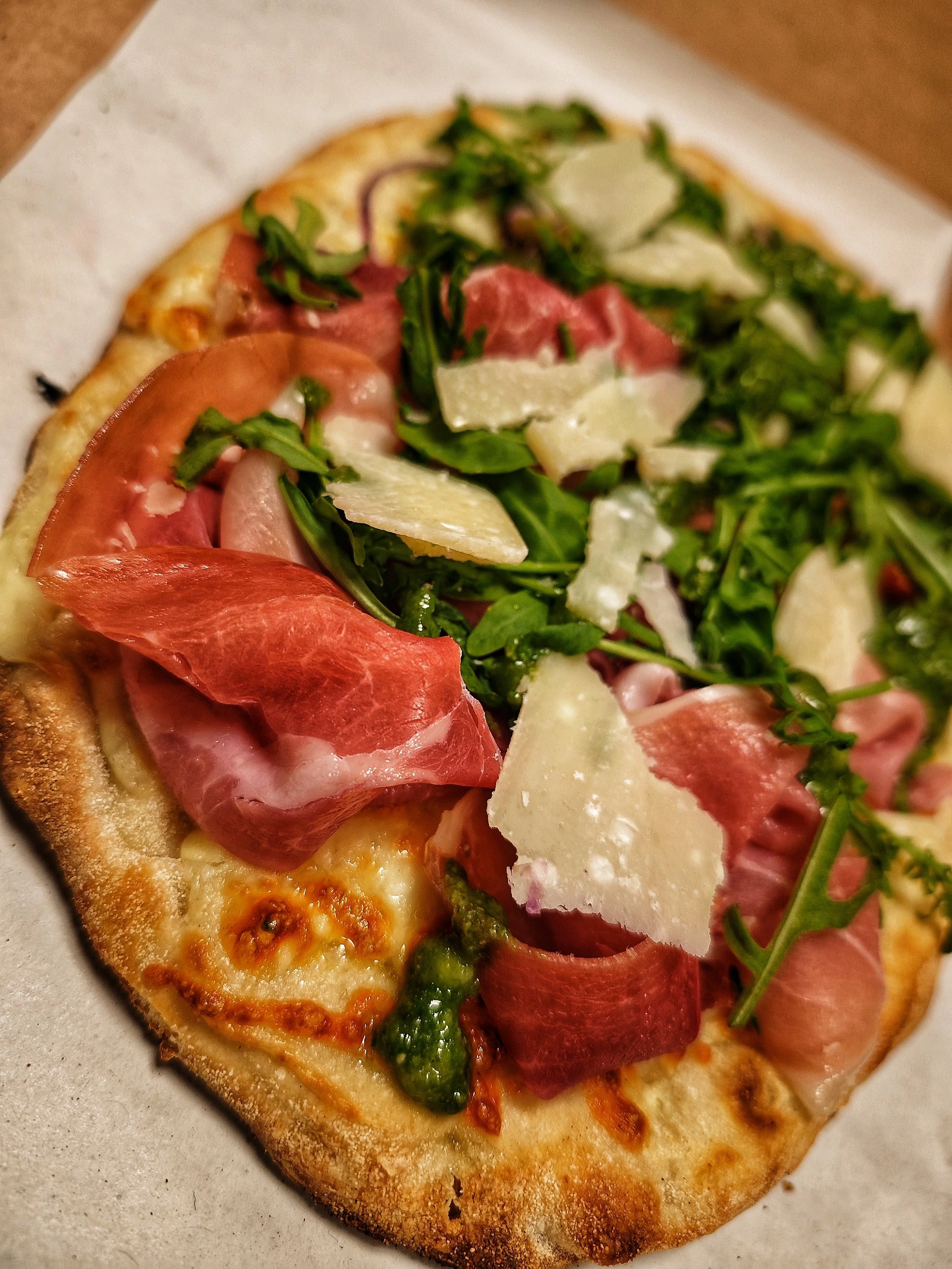 Eine Pizza mit Tomaten, rohem Schinken, Rucola, Parmesan und grüner Sauce
