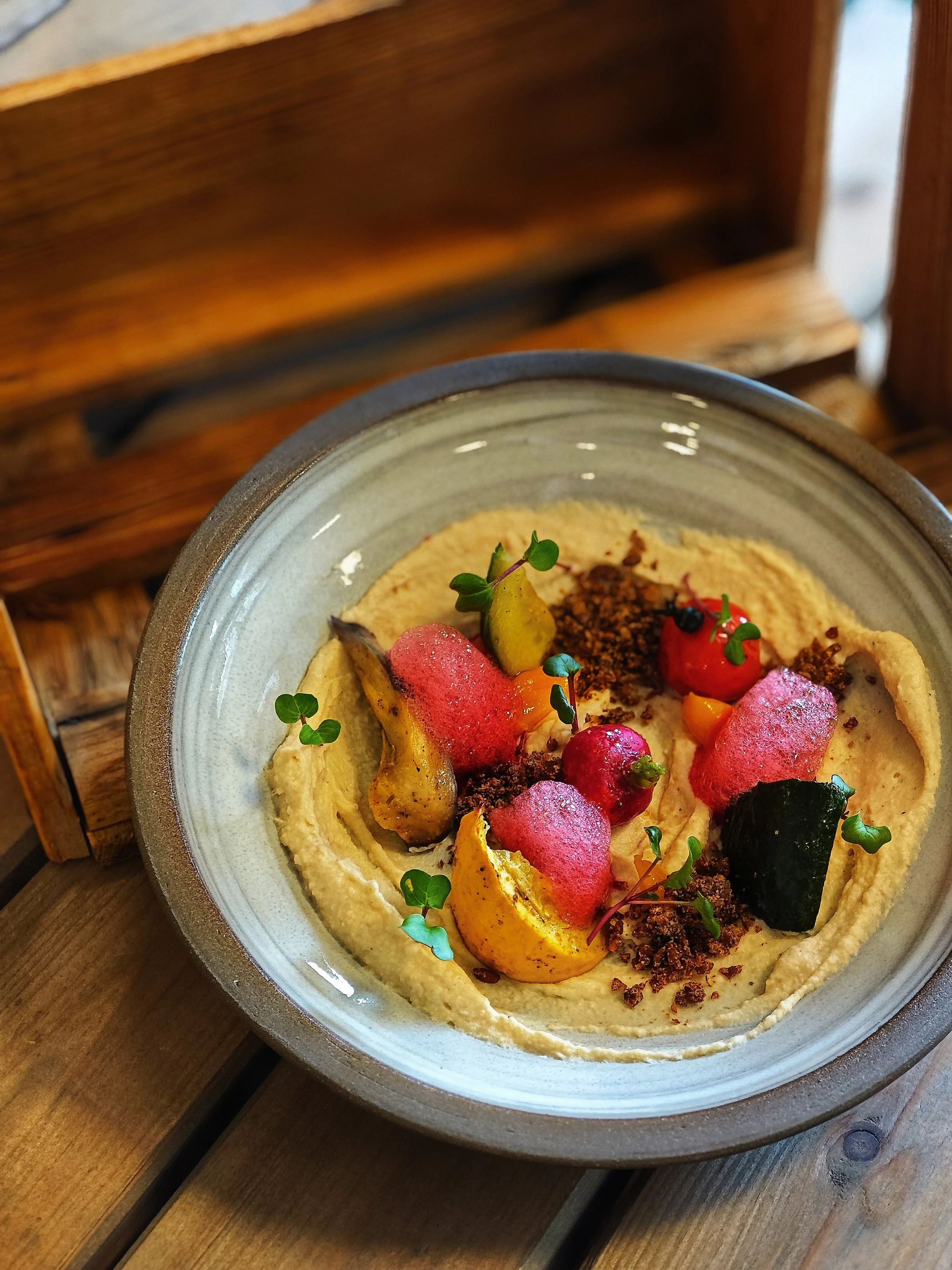 Ein Teller mit Hummus, garniert mit geröstetem Gemüse, roten Radieschen, Kaviar, frisch gehackten Kräutern und Gewürzen.