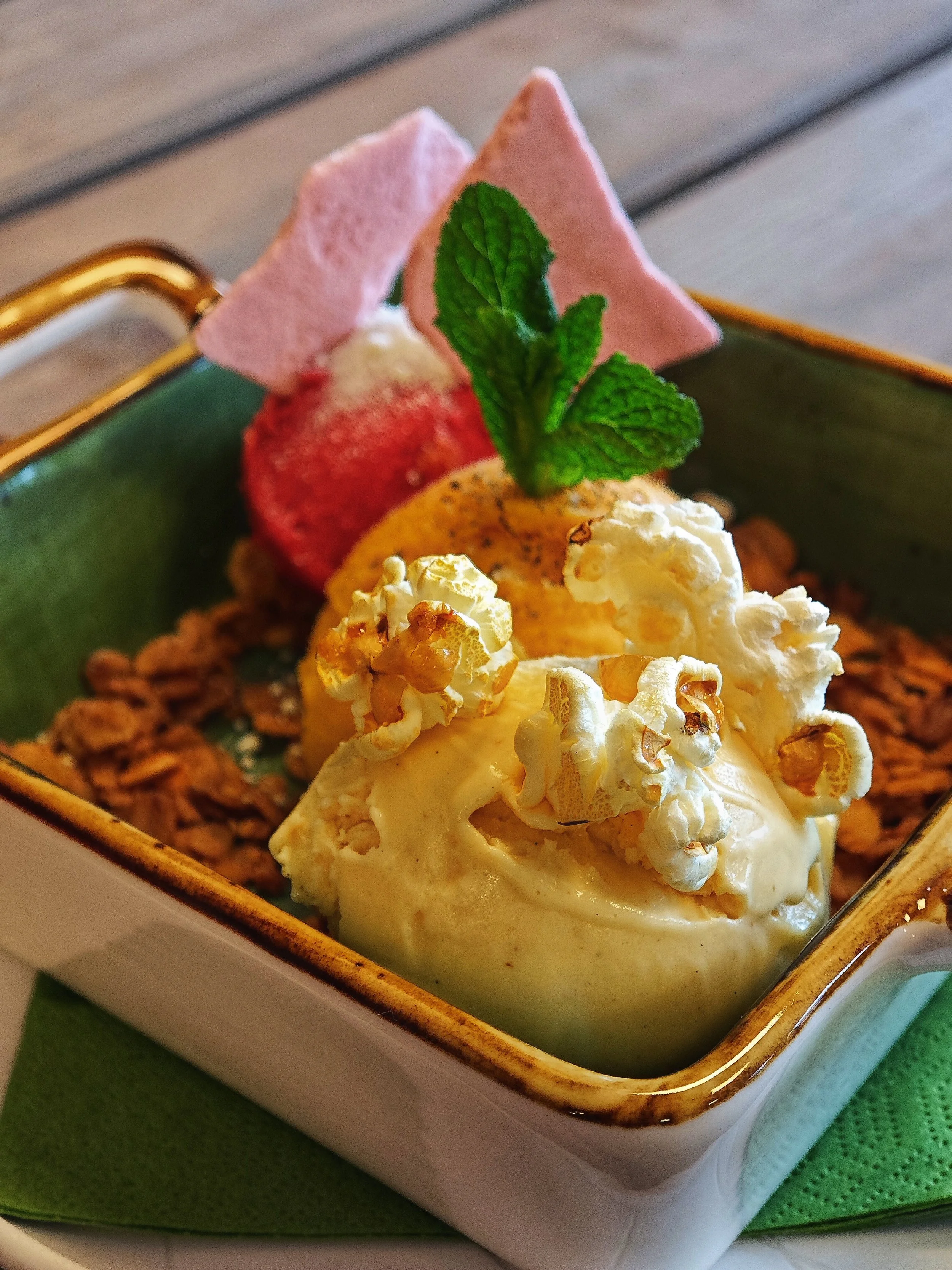 Eiscreme mit Popcorn, Minzblättern, Erdbeere und Waffelröllchen in einer Schale