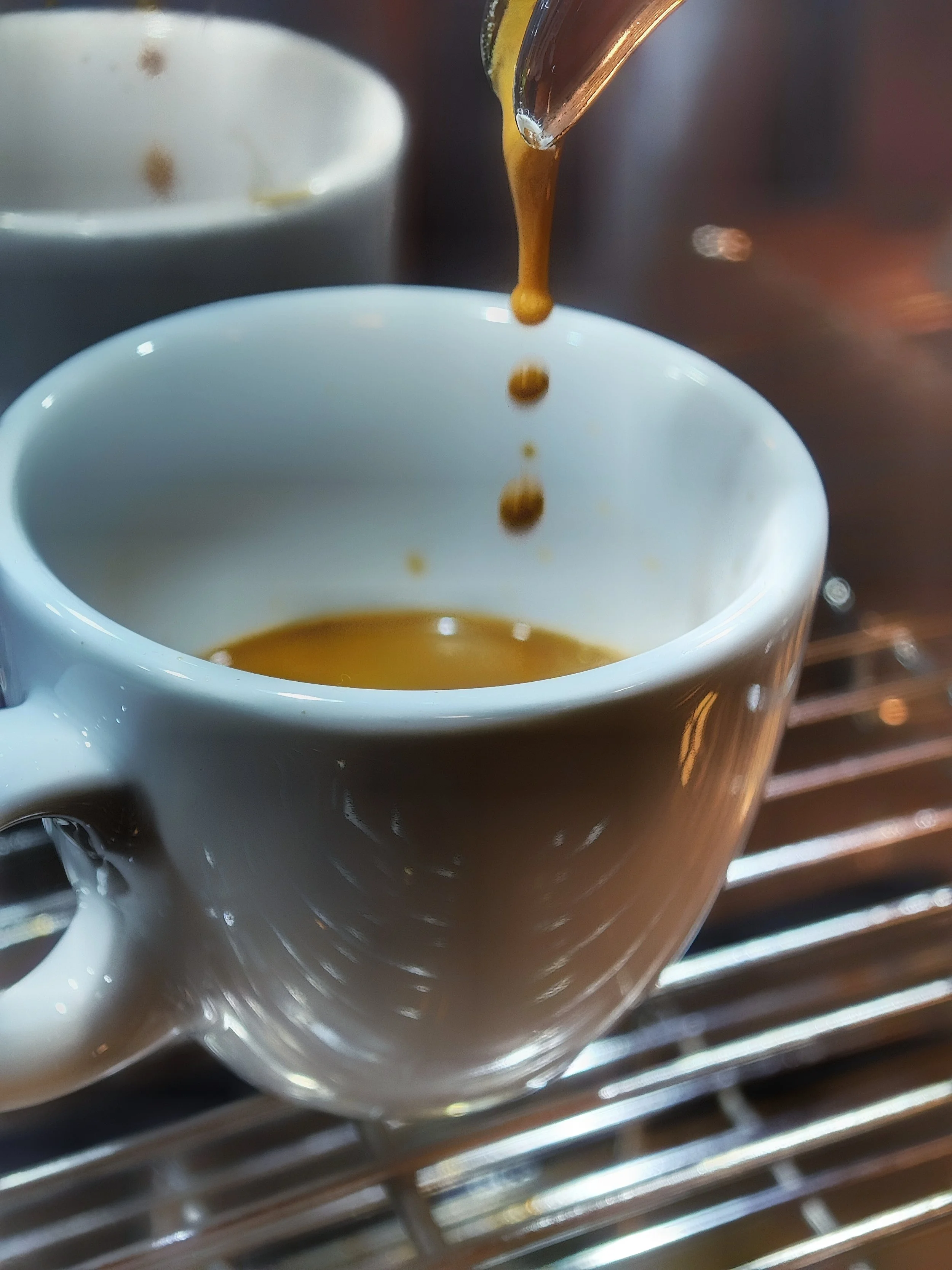 Nahaufnahme einer Espressotasse, aus der frisch gebrühter Espresso in eine weiße Tasse fließt.