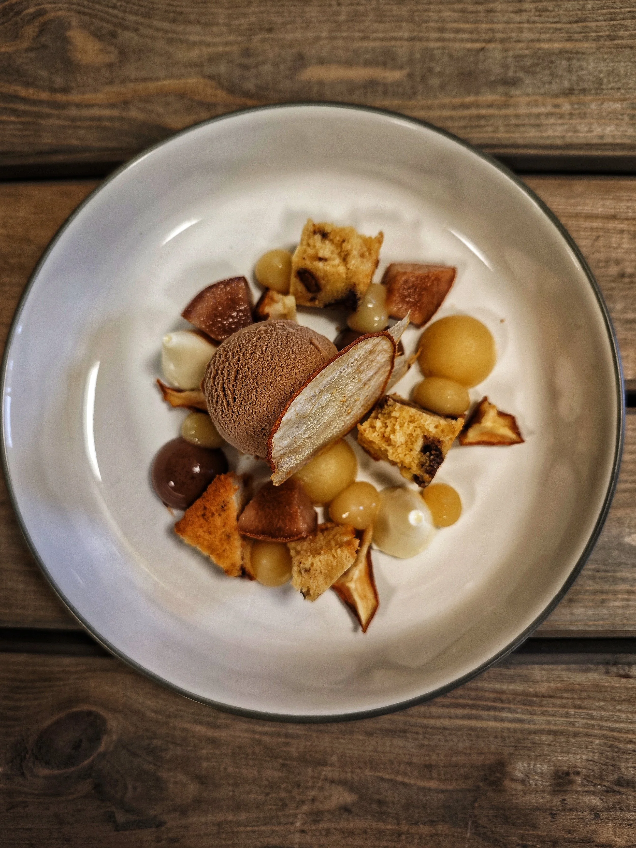 Dessert mit Eiskugeln, kleinen Keksstücken und Früchten auf weißem Teller