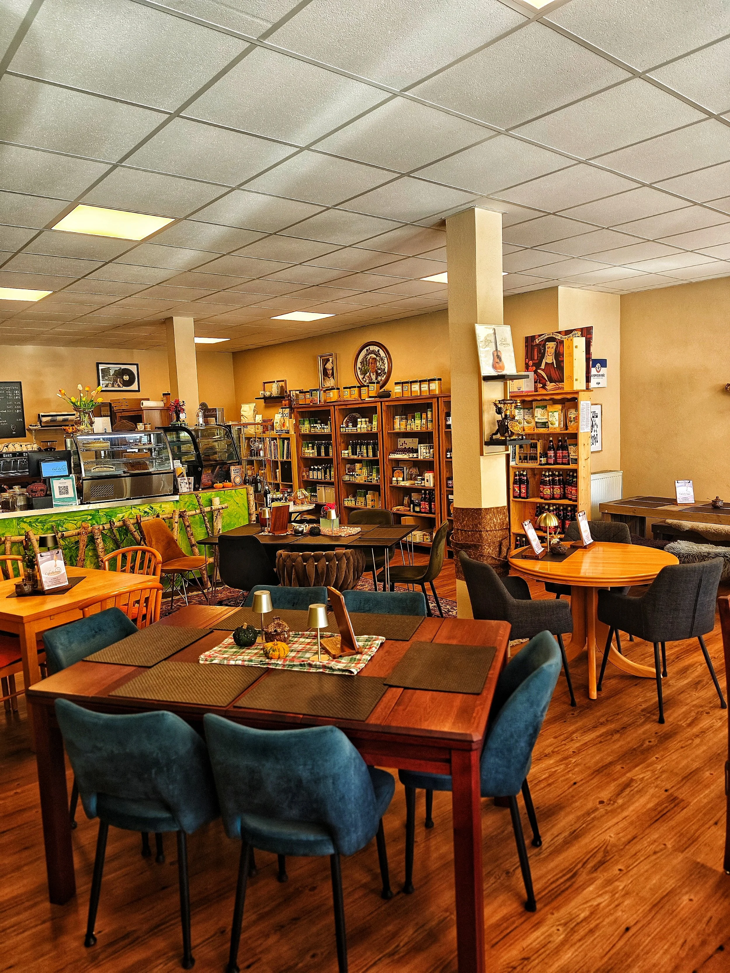 Innenansicht eines gemütlichen Cafés mit Holztischen, bequemen Stühlen, Bücherregalen und Dekorationsgegenständen.