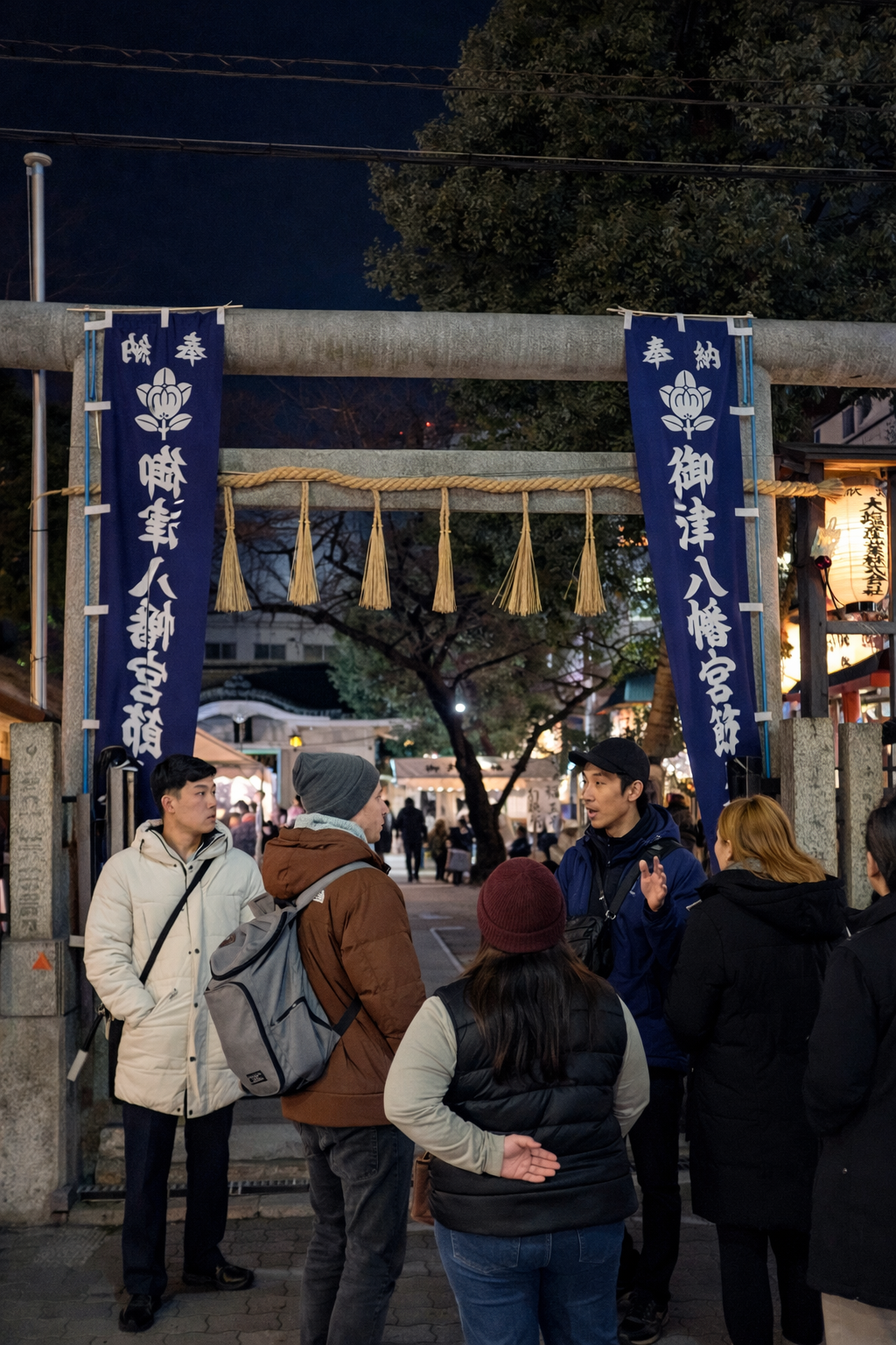 A group of people talking under a Japanese torii gate at a night market or festival.