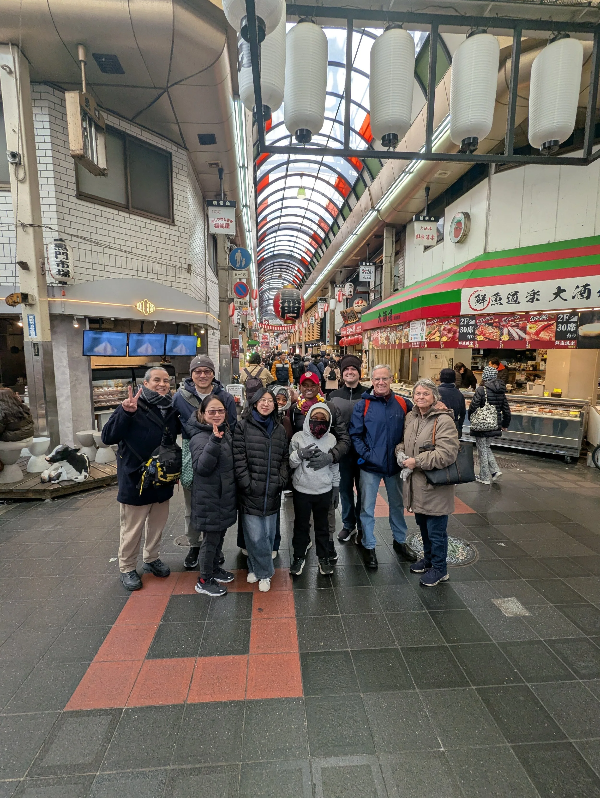 A group of people posing for a photo inside a covered shopping street with lanterns and shops in the background.