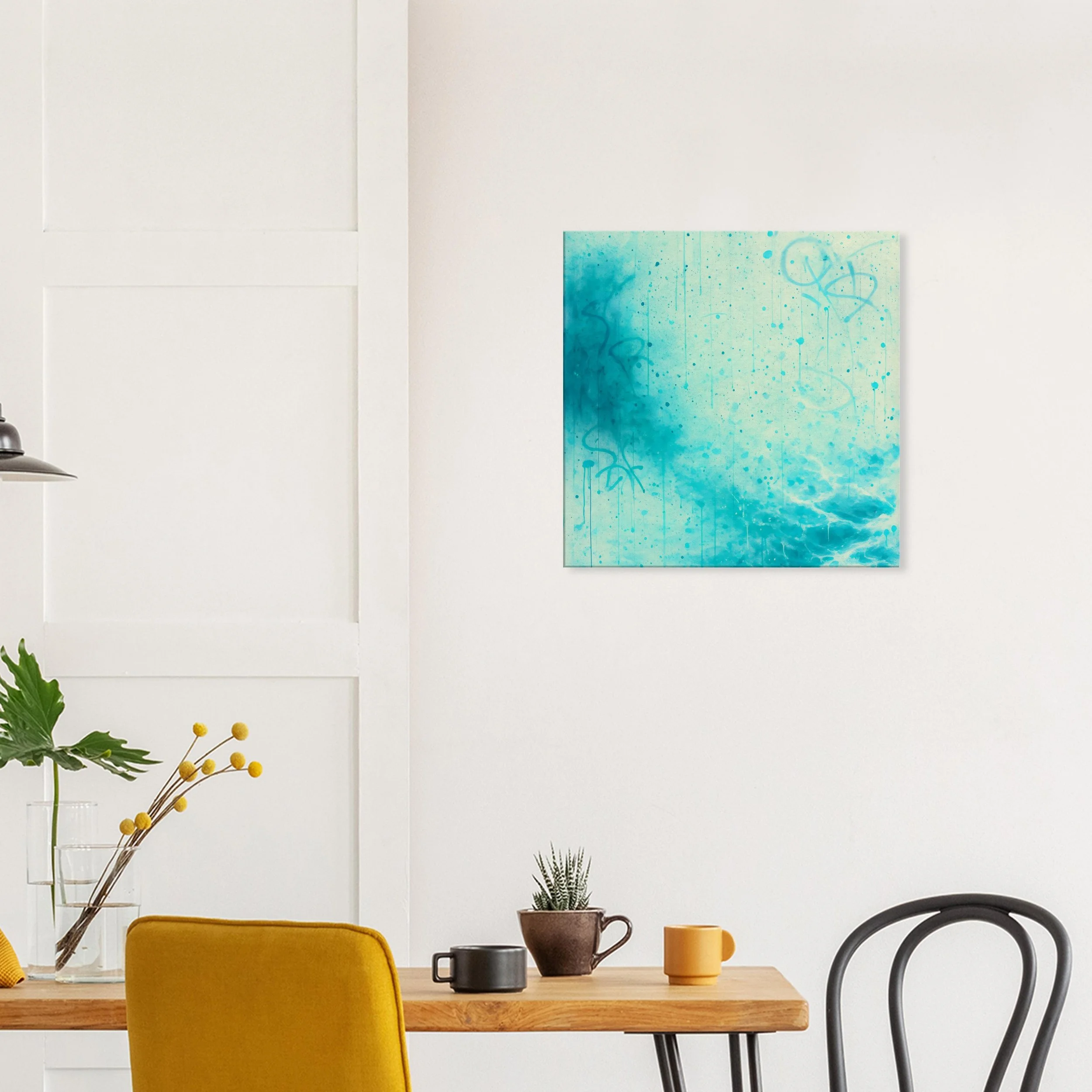 A modern dining area with a wooden table, yellow chair, black chair, a small potted plant, black and yellow mugs, and a large artwork with blue tones on a white wall.
