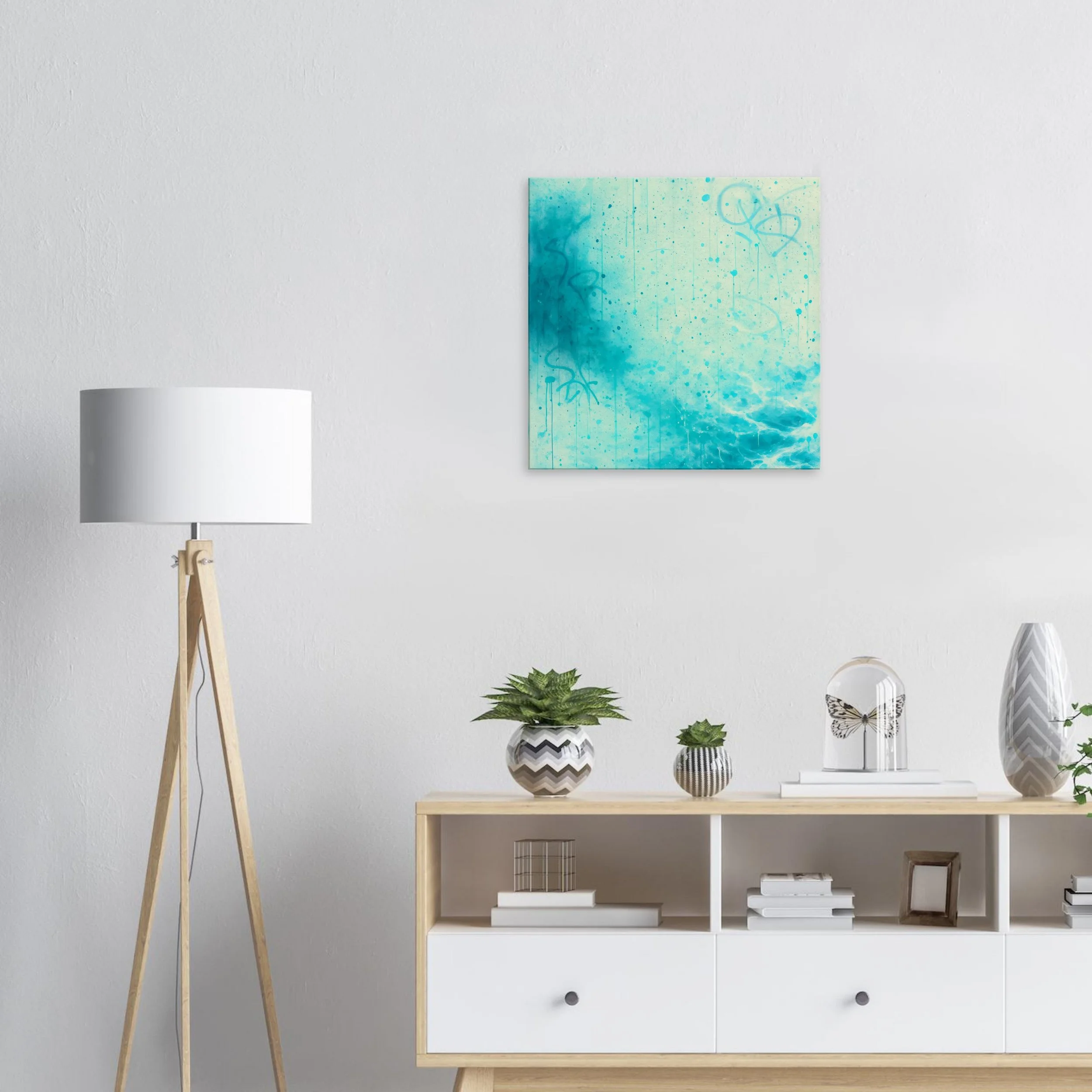 Modern living room with a white wall, a standing wooden tripod lamp, a wooden console table with white drawers, and decorative items including potted plants, books, and vases. A blue abstract painting hangs on the wall.