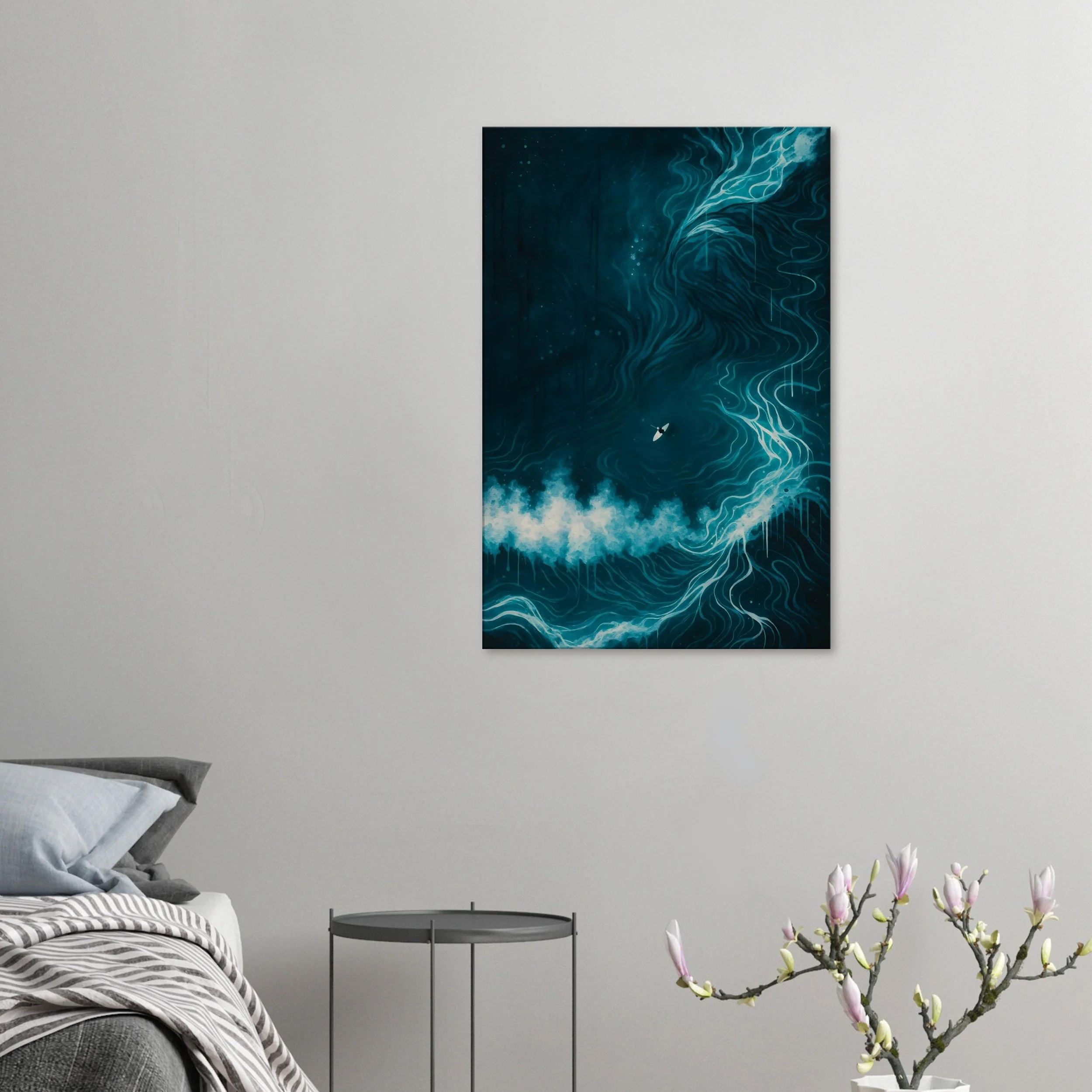Modern bedroom with a gray bed, striped blanket, and pillows, a small round black side table, and framed abstract blue and white artwork on a white wall, with a flowering branch in the foreground.