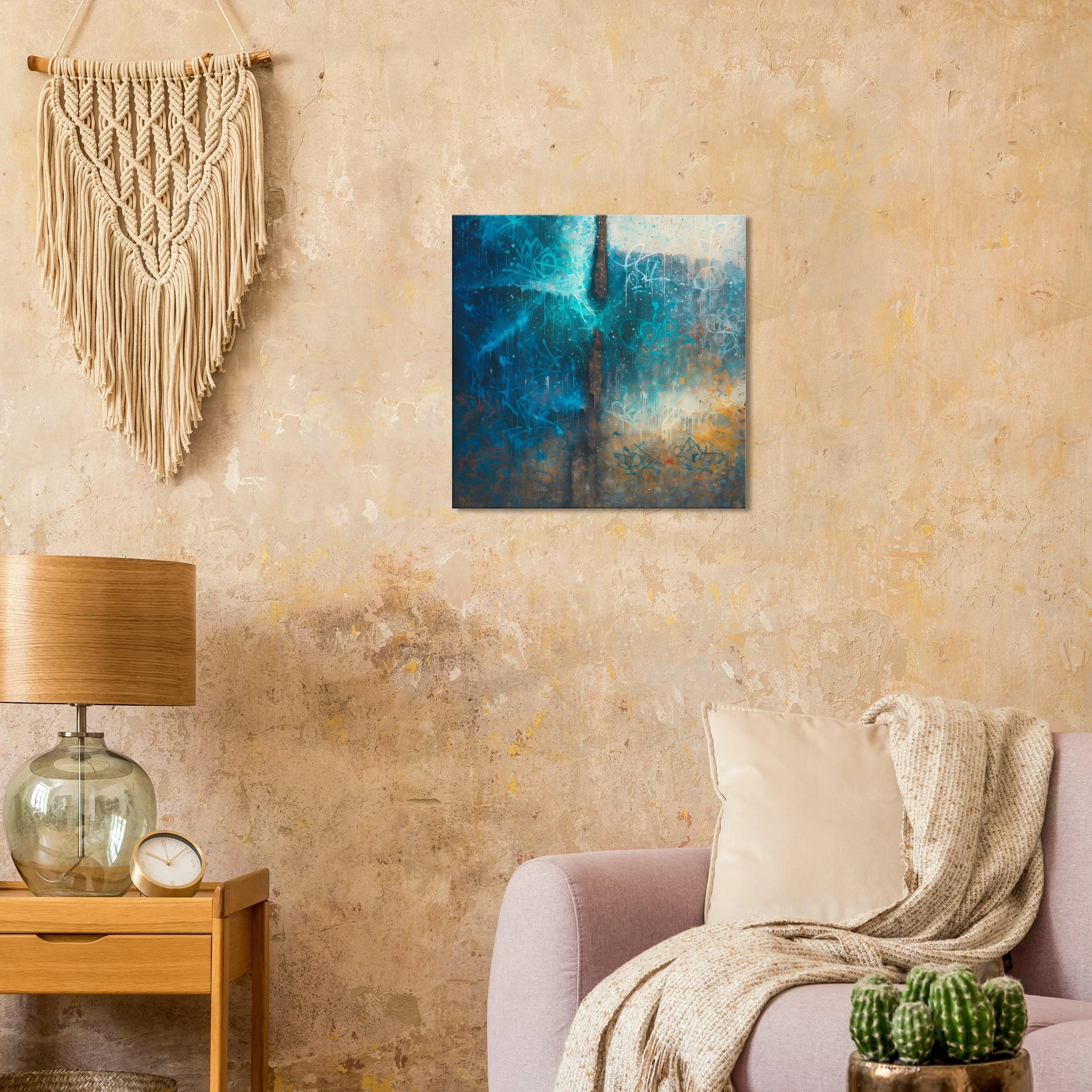 A cozy living room corner with a textured beige wall, a pastel pink couch with a cream pillow and a blanket, a wooden side table with a glass lamp and a clock, a green cactus plant, a blue abstract painting on the wall, and a macrame wall hanging.