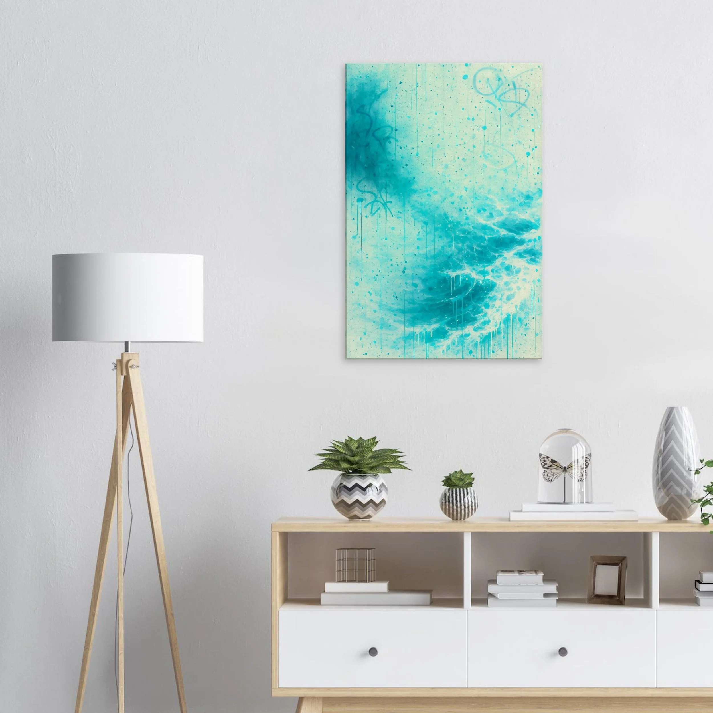 A modern living room wall with a white background, decorated with an abstract blue and teal painting. A white floor lamp with wooden legs stands to the left, and a light wood sideboard with decorative items, including potted plants, vases, books, and