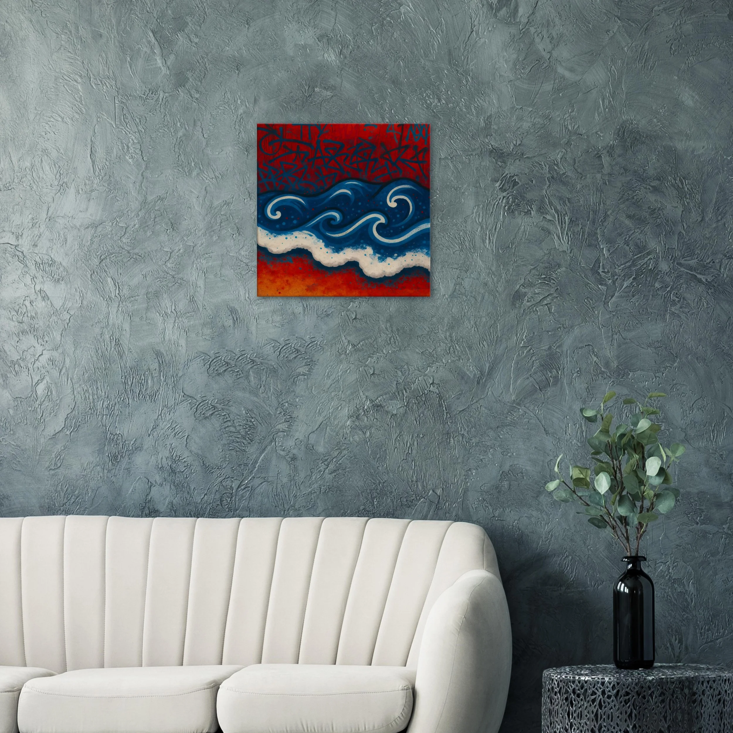 A small colorful painting of blue and white waves on a red background hanging on a textured gray wall in a room with a white sofa and a black vase with green leaves on a side table.