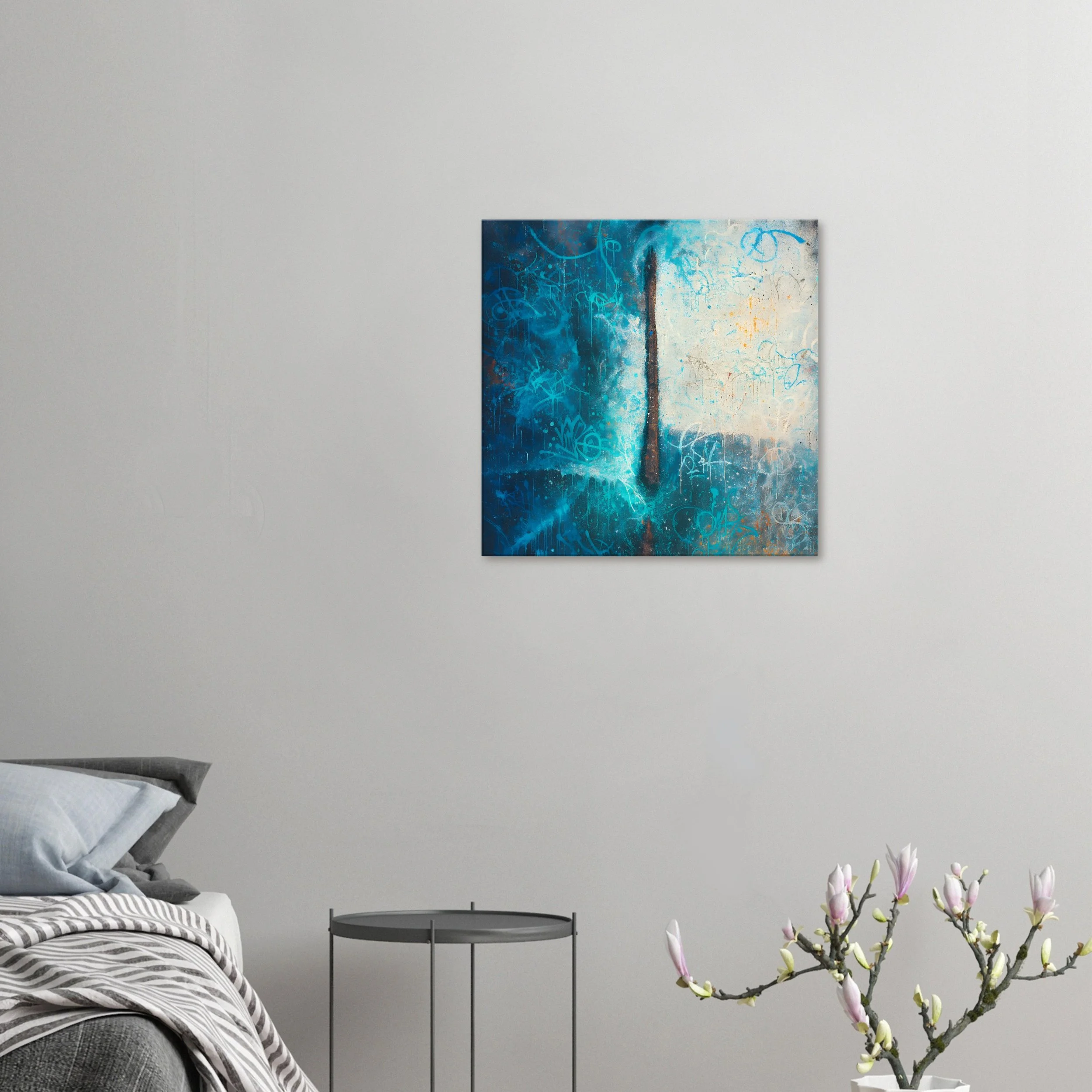 A contemporary bedroom with a bed on the left, a small round black side table, and a white vase with pink magnolia flowers on the right. On the white wall, there is a square abstract painting with shades of blue, white, and hints of orange and brown.