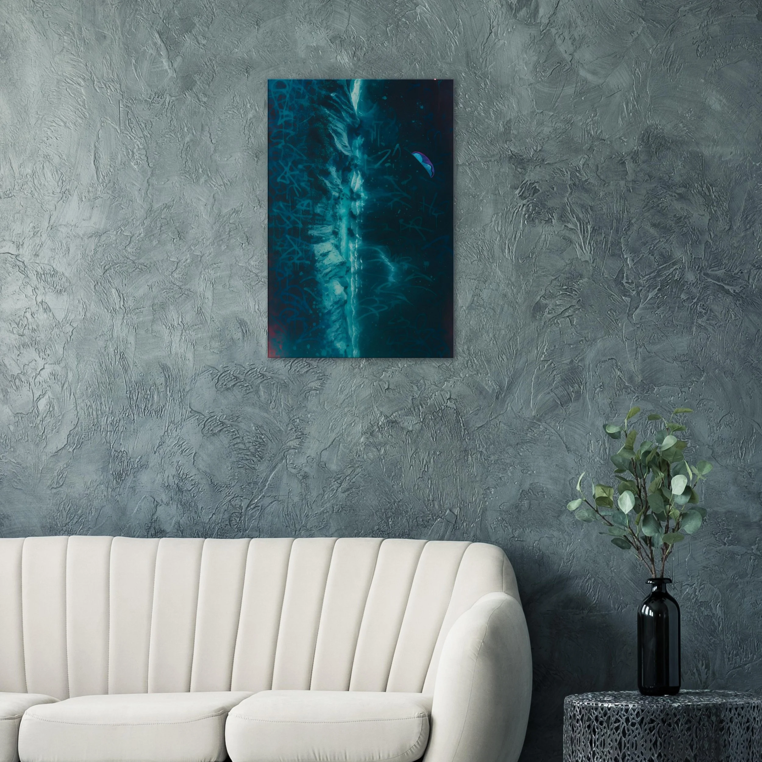 Modern interior with a textured dark gray wall, a white curved sofa, a black vase with green leafy plant, and abstract blue artwork hanging on the wall.