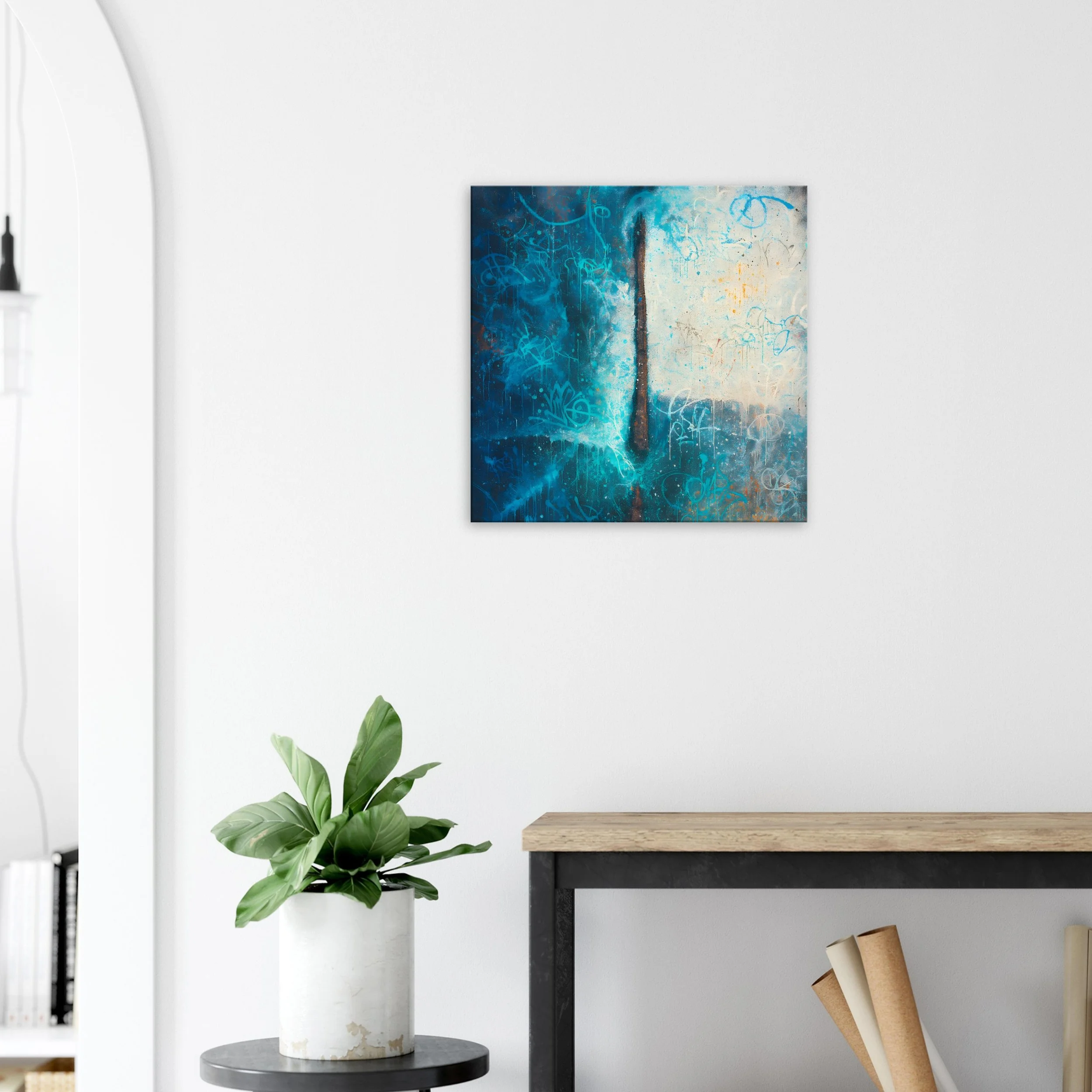 Abstract blue and white artwork on a white wall above a wooden table and a green houseplant in a white pot.