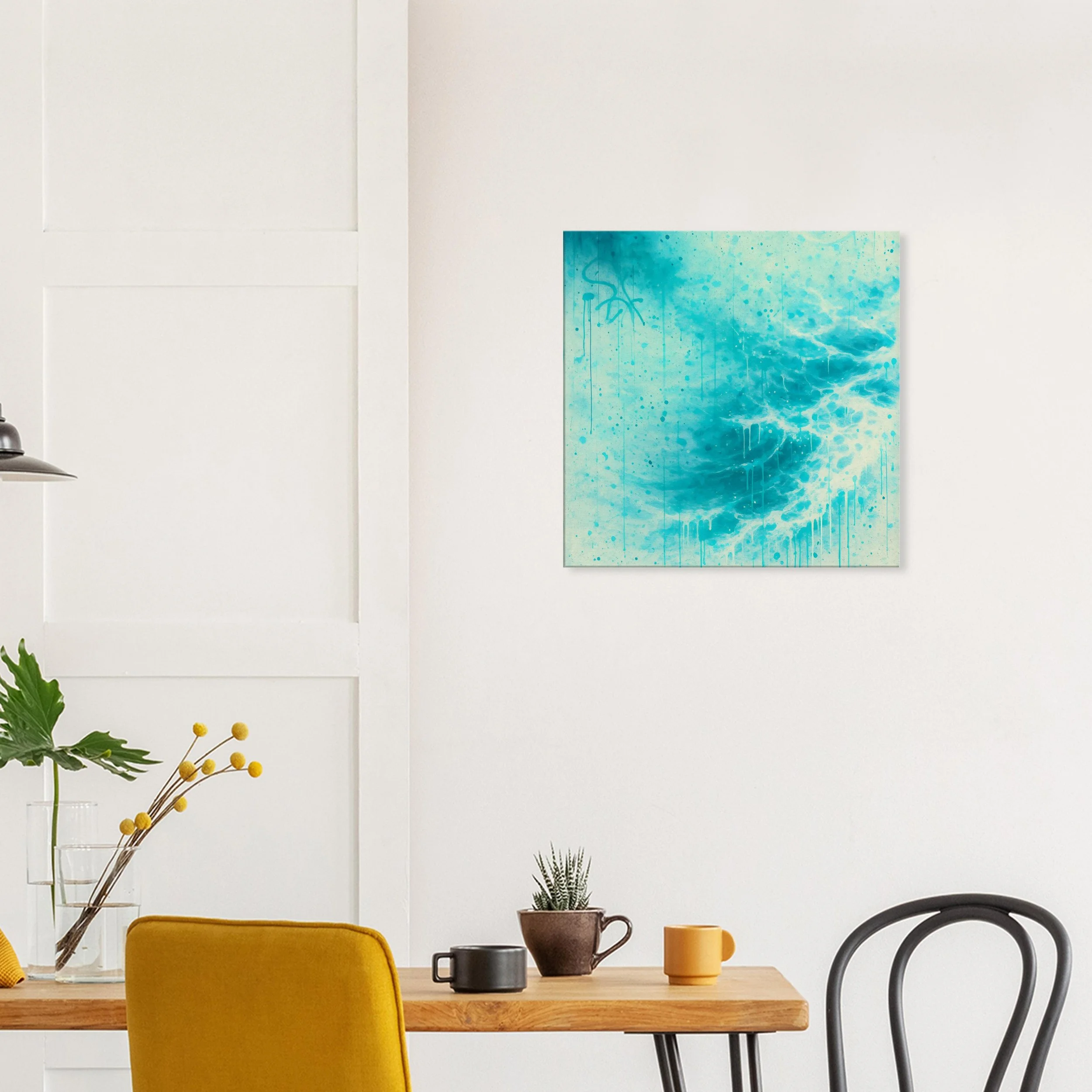 A contemporary dining or living space with a wooden table, yellow chair, and black and yellow mugs. There are plants, one with large green leaves in a glass vase and a small potted succulent. A blue abstract painting of ocean waves hangs on a white w