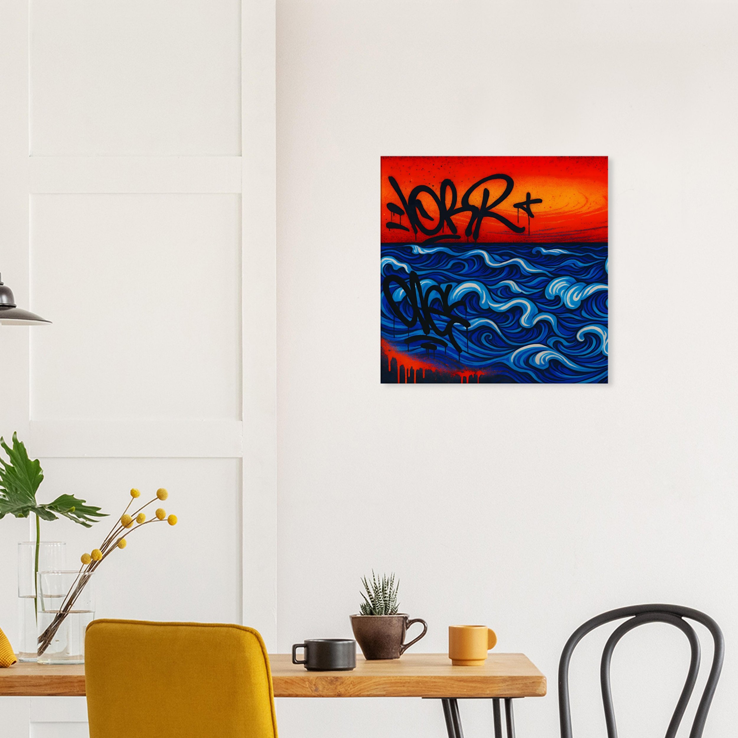 An interior room with a white wall and minimalist decor, featuring a colorful painting of a sunset over waves, with graffiti-style text on the artwork. A wooden table holds a plant in a pot, a black cup, and a yellow mug, with a yellow chair and a bl