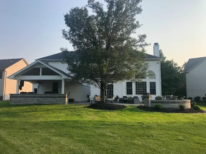 Backyard of a modern house with a large tree, patio furniture, and a well-maintained lawn.
