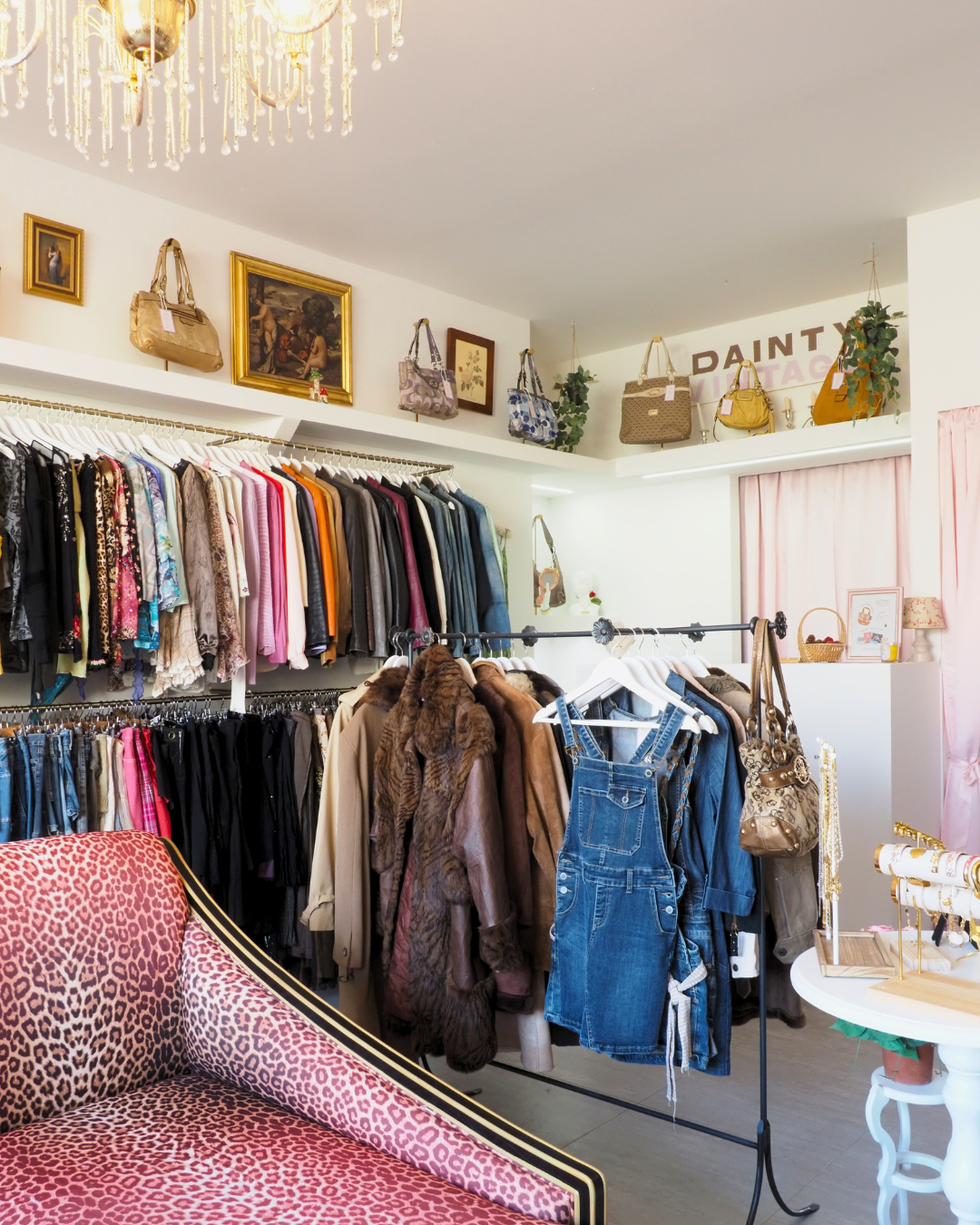 Dainty Vintage - a vintage store in Malta with racks of colorful clothes, Vintage Coach handbags, and accessories, decorated with artwork, plants, and a chandelier.