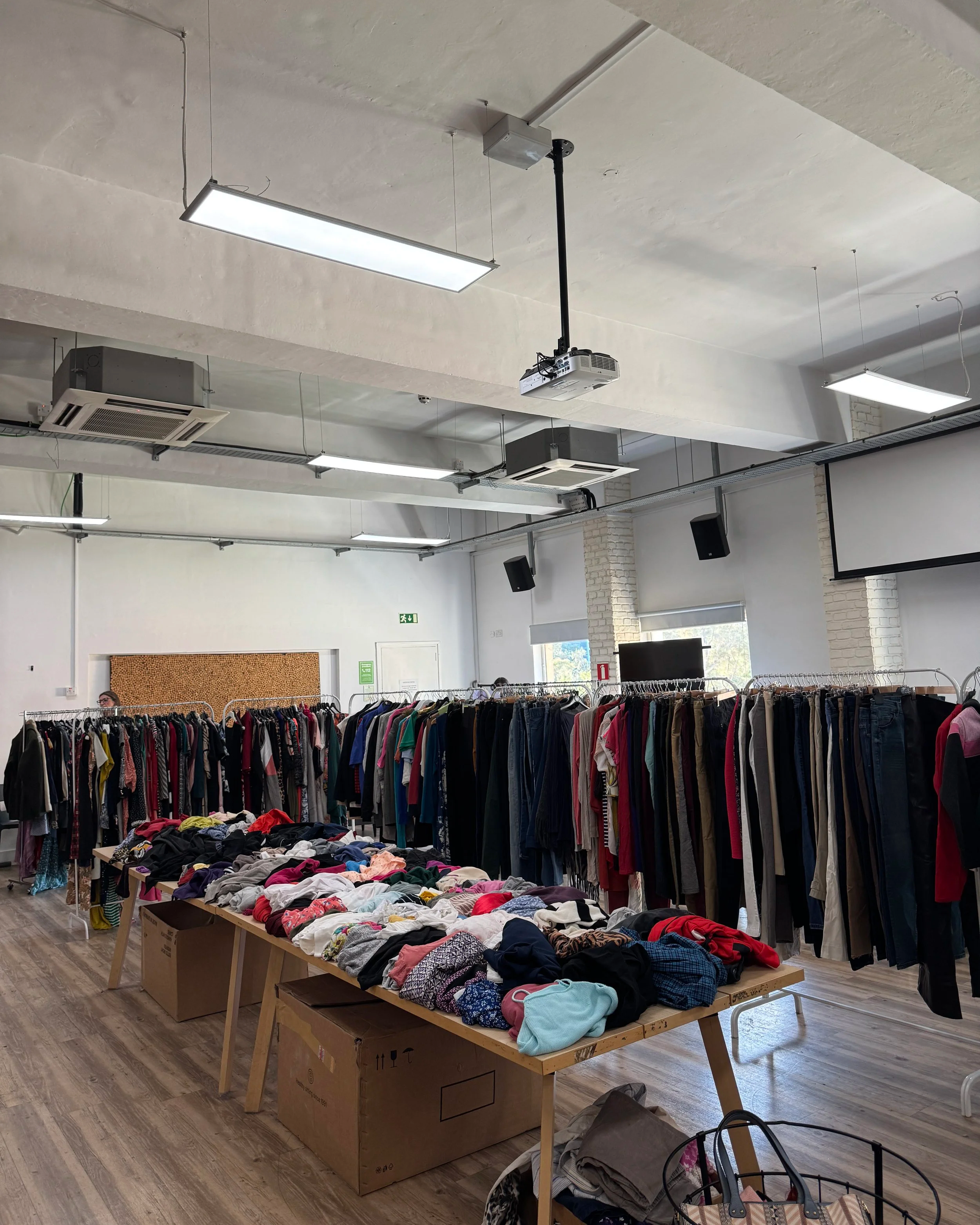 Indoor Kilo sale in Malta with tables of folded clothes and racks of hanging clothes in a well-lit room.