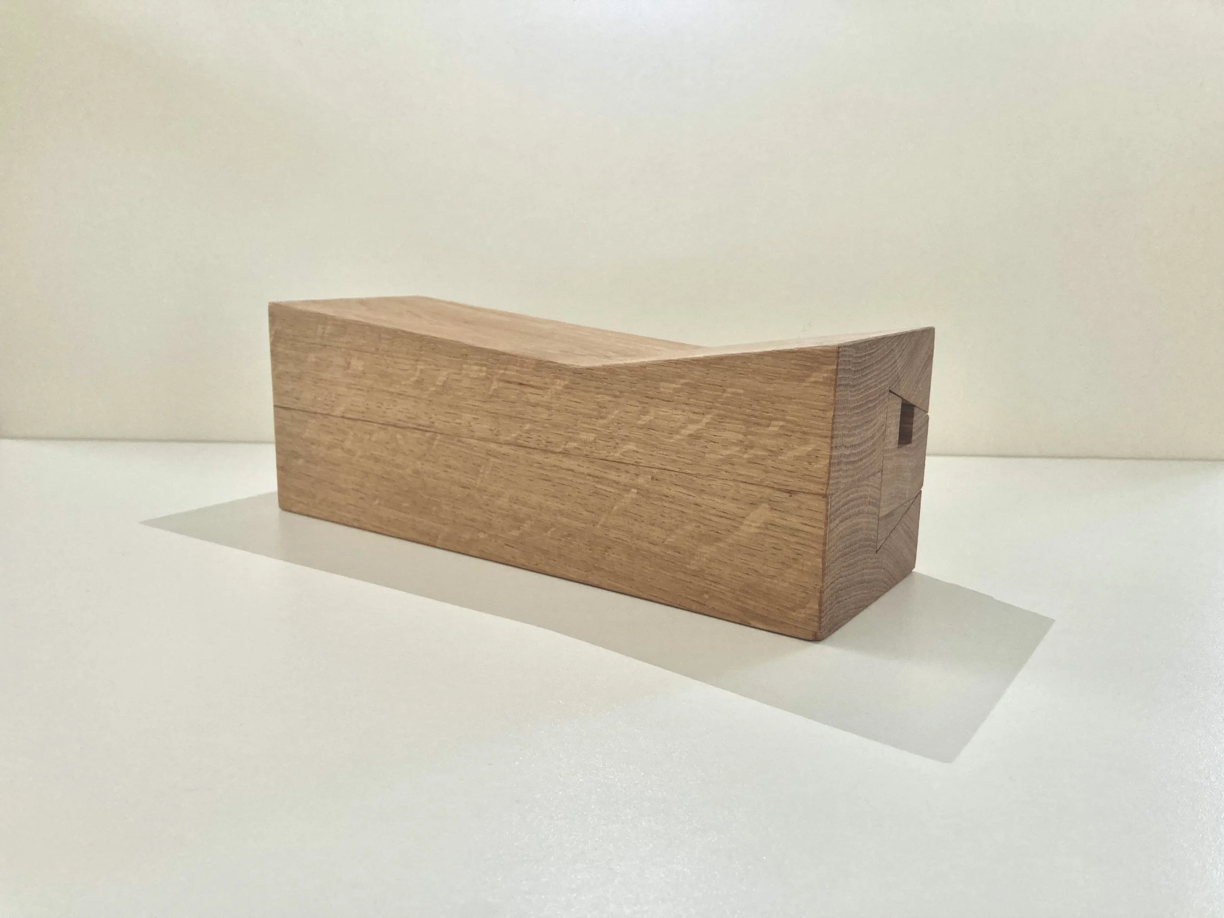 Een houten blok met een spleet en een uitsparing, geplaatst op een witte ondergrond en tegen een witte achtergrond.