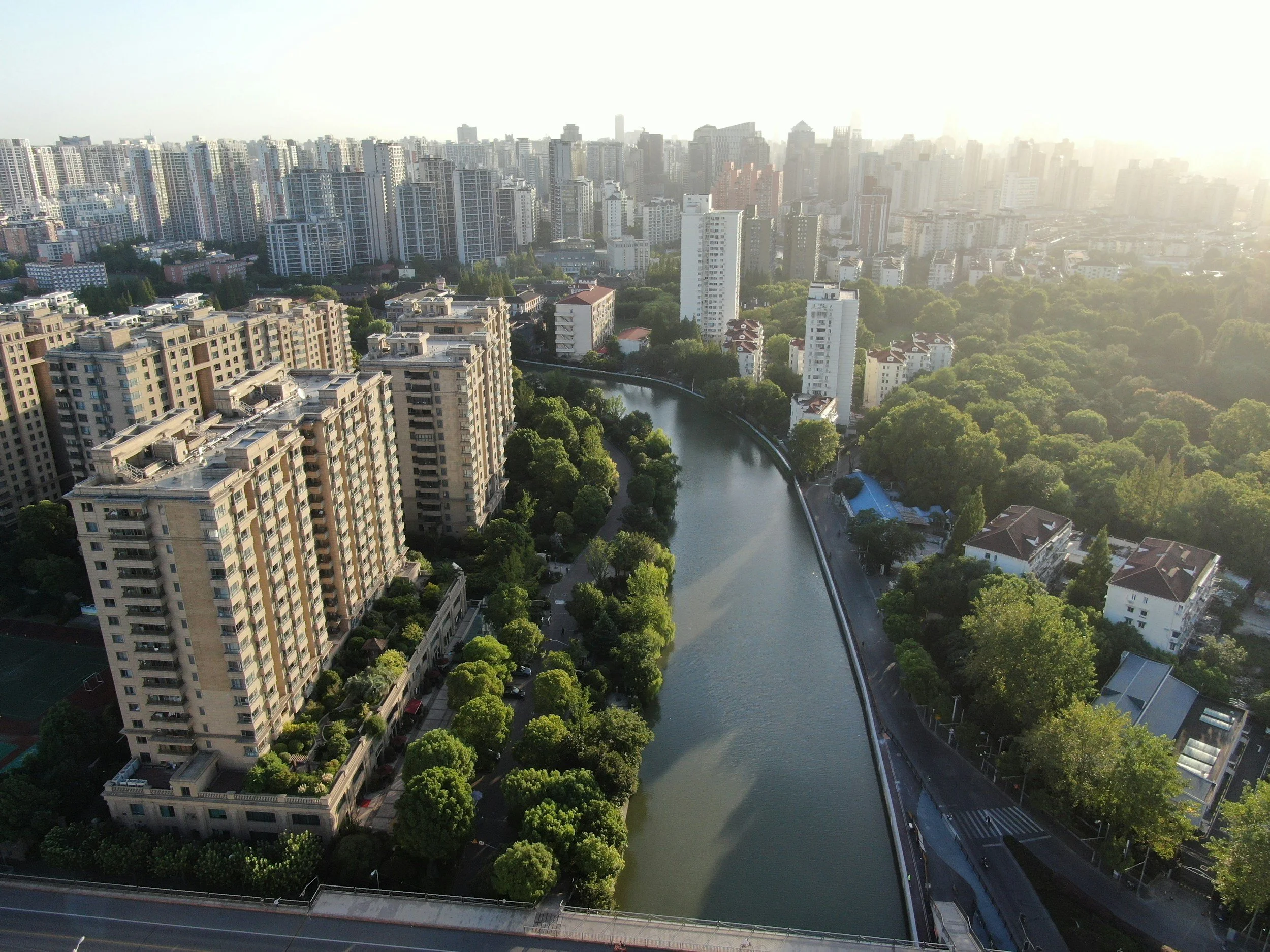 Aerial view of a city with tall buildings, a river, and green trees, taken at sunset.
