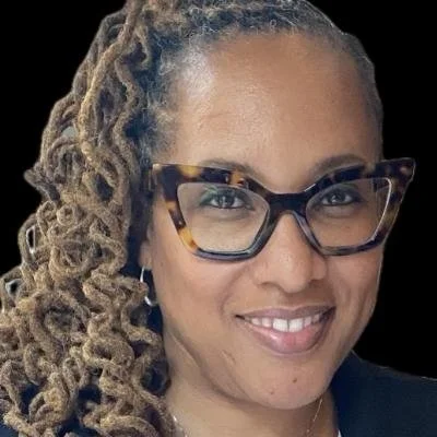 Close-up portrait of a smiling woman with curly hair and glasses against a black background.