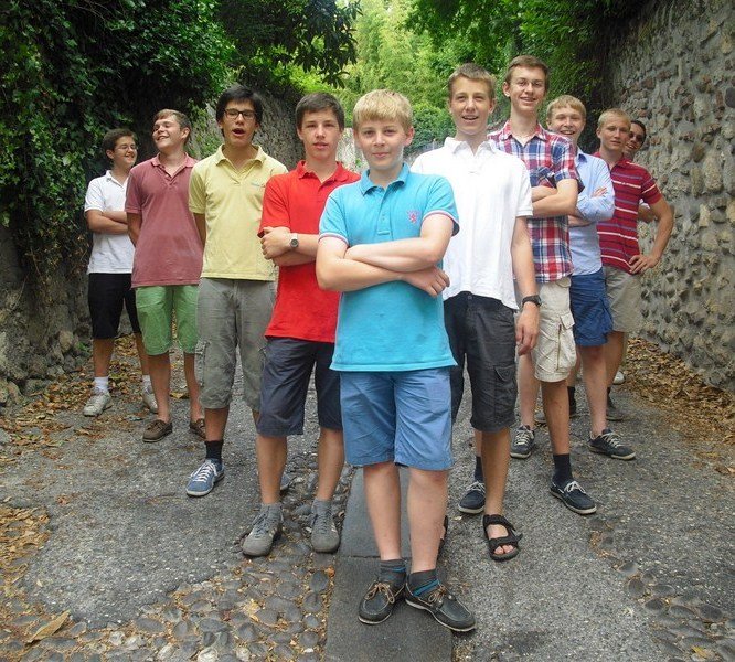 Gruppe junger Jungen läuft auf einem Weg im Freien, umgeben von Bäumen und einer Mauer im Hintergrund.