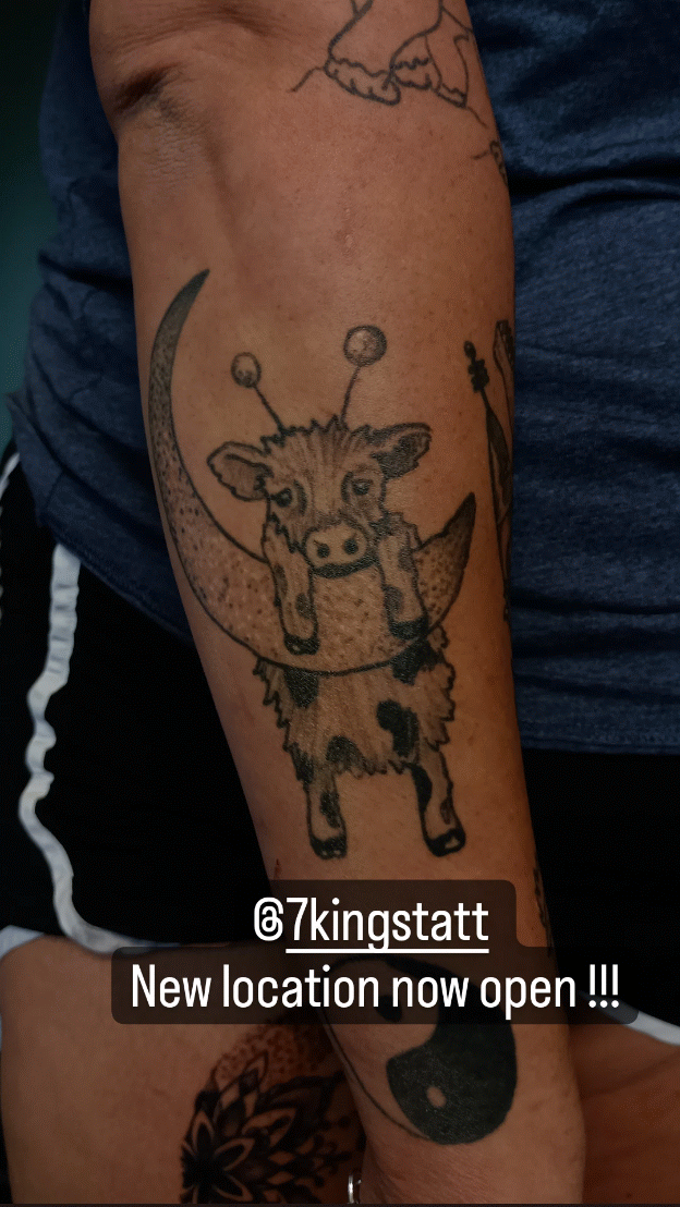 Tattoo of a playful moon with a cute calf hanging on it, on a person's arm.