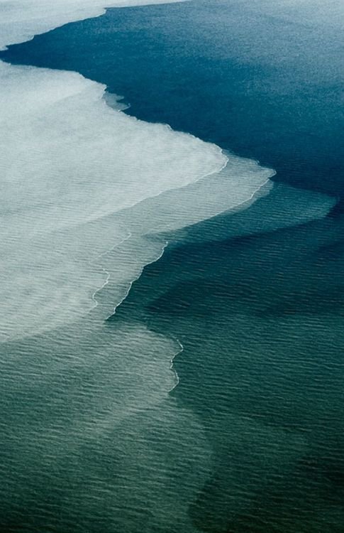 Aerial view of ocean waves from an airplane window with white surf breaking along a shoreline.