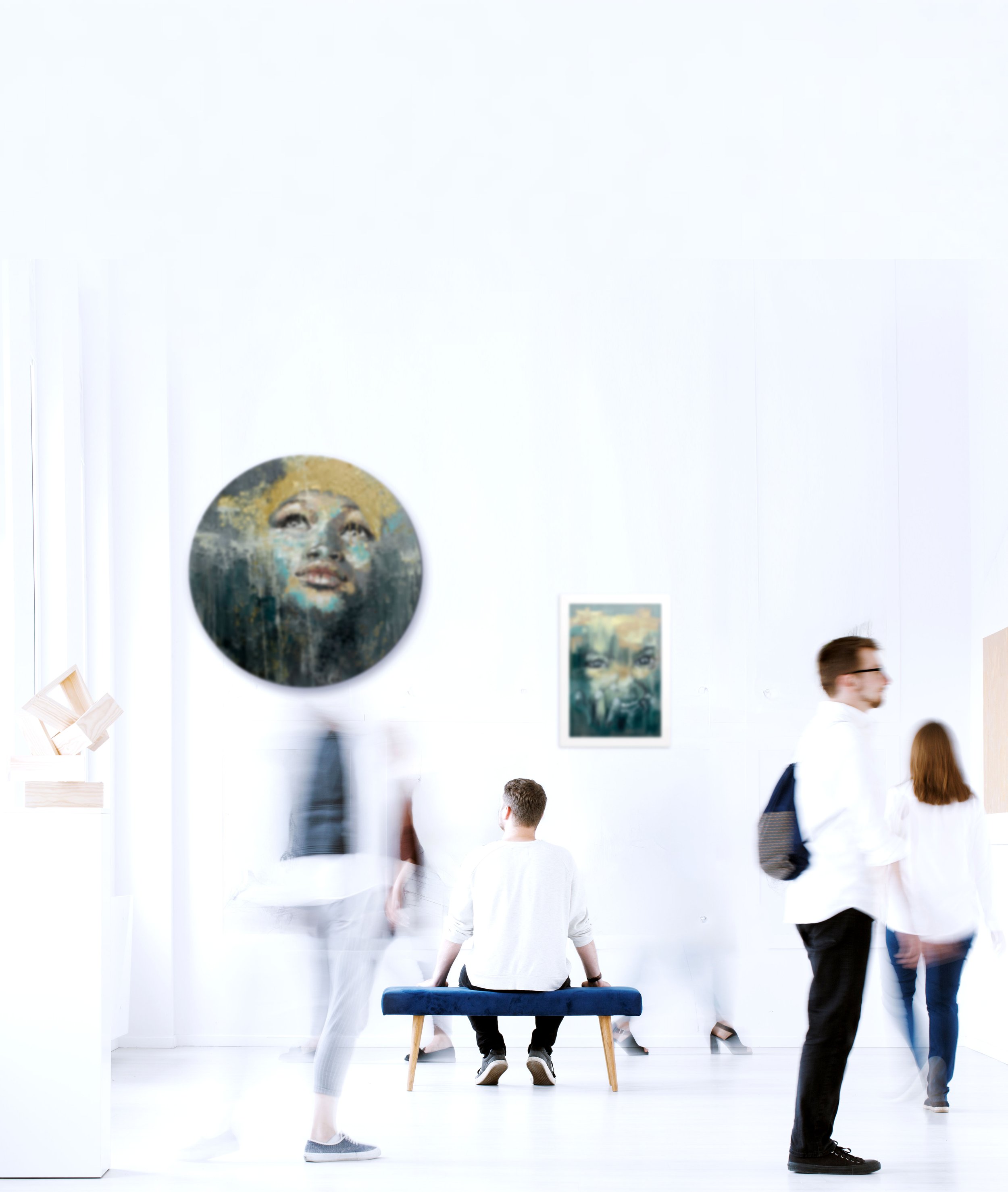 People in an art gallery viewing modern paintings by Elize Roelofse on white walls, with some walking and one person sitting on a bench.