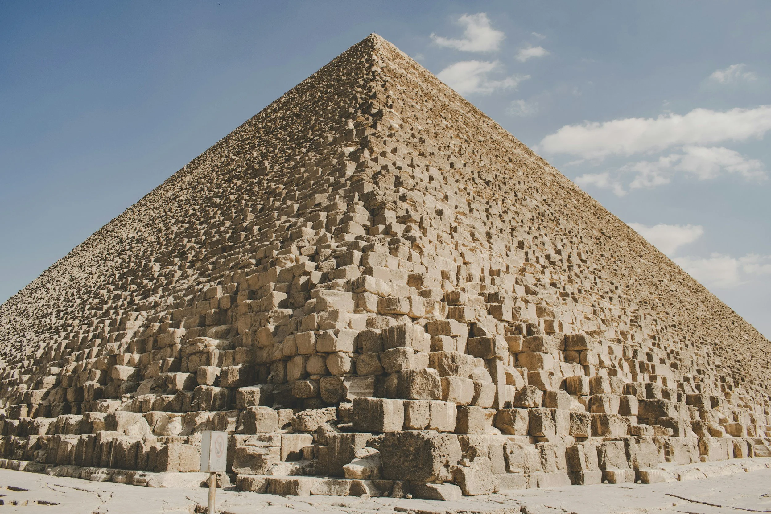 The Great Pyramid of Giza under a blue sky with scattered clouds.