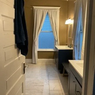 Bathroom with a window, blue vanity, mirror, and light fixture, beige walls, and tiled floor.